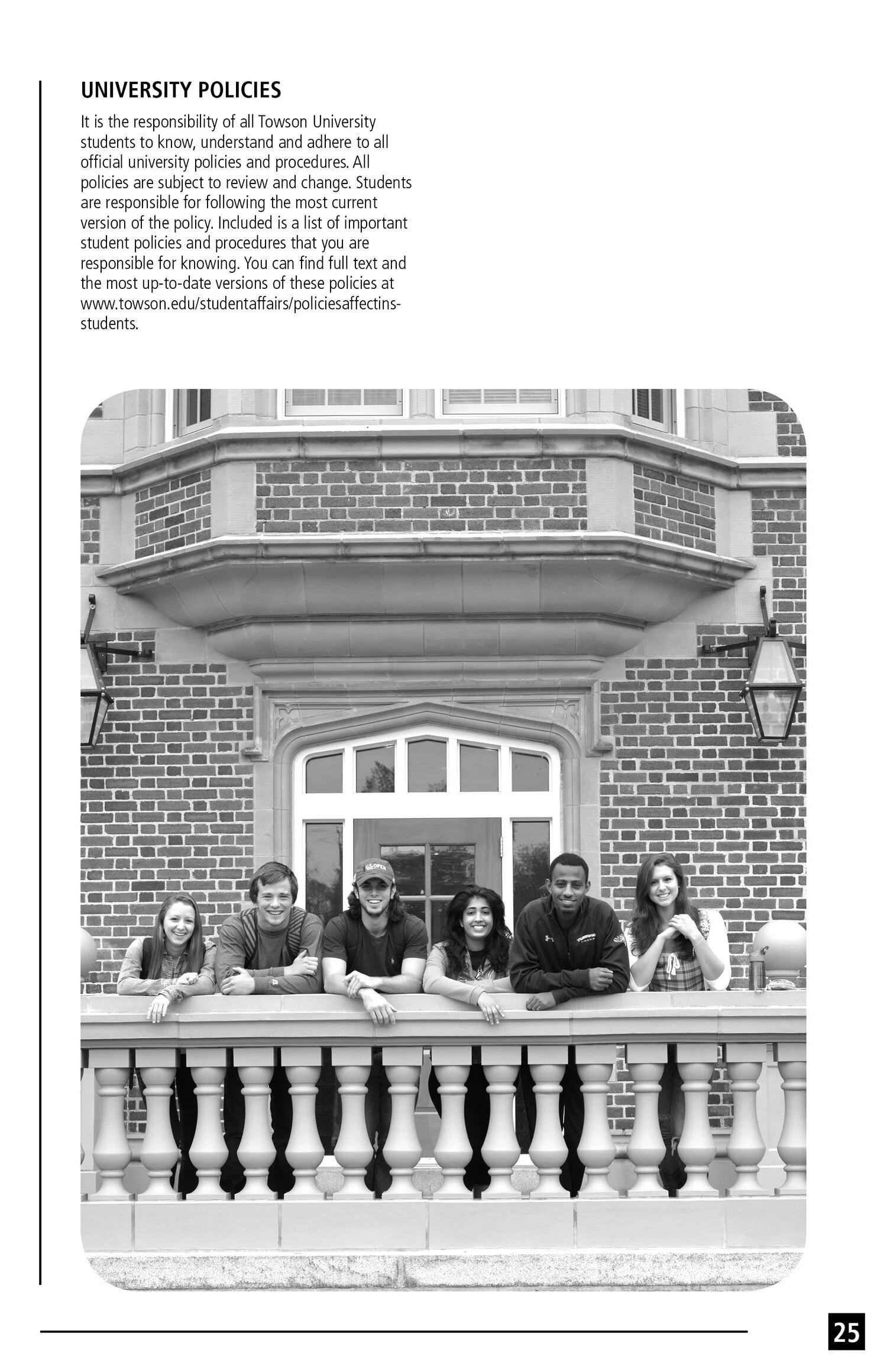 Black and white photo of six students leaning on a balcony railing in front of a brick building with large windows and an arched doorway, smiling at the camera.