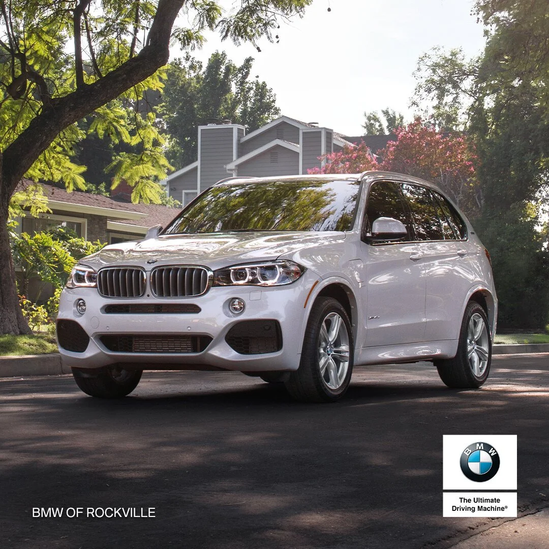 A white BMW SUV parked on a residential street with trees and houses in the background.
