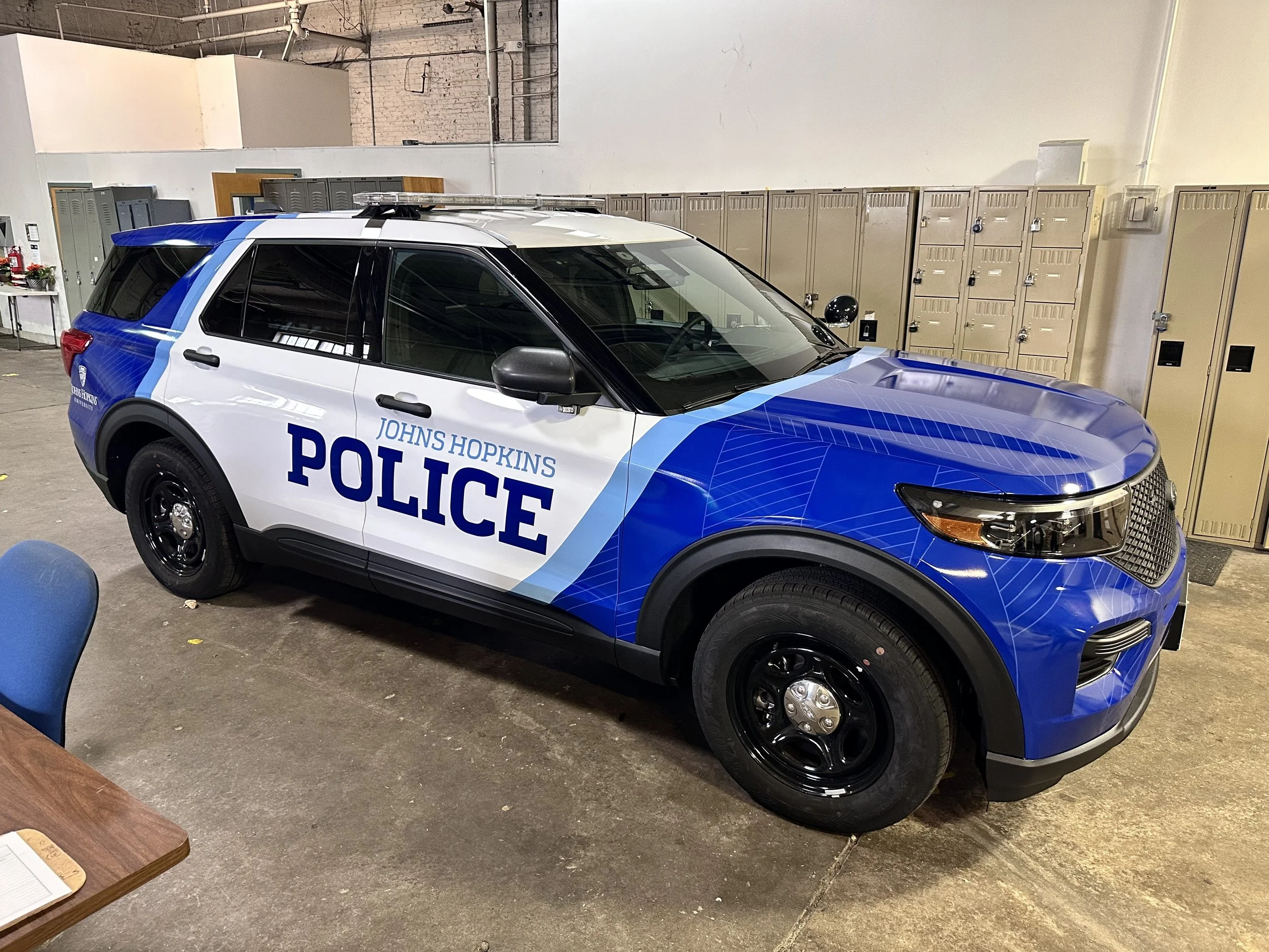 Blue and white Johns Hopkins Police SUV parked indoors, with lockers and a table in the background.