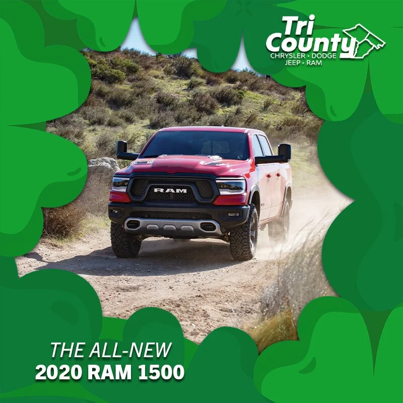 A red 2020 RAM 1500 truck driving on a dirt trail through a desert landscape with dry bushes and hillside in the background, surrounded by a green decorative border with the words "Tri County Chrysler Dodge Jeep Ram" in the top right corner and "The 