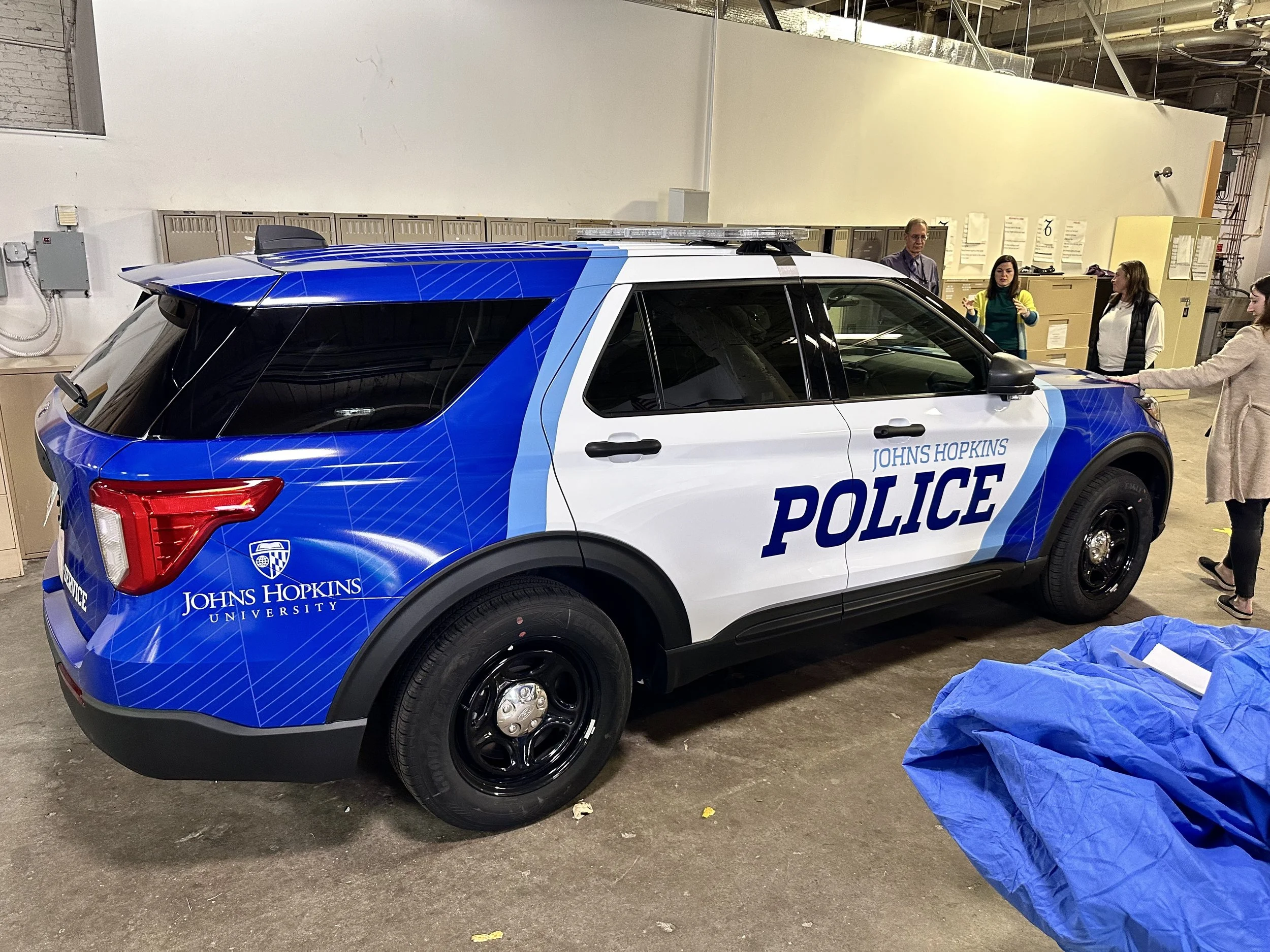 A police SUV with Johns Hopkins University branding parked indoors, with a group of people standing nearby.