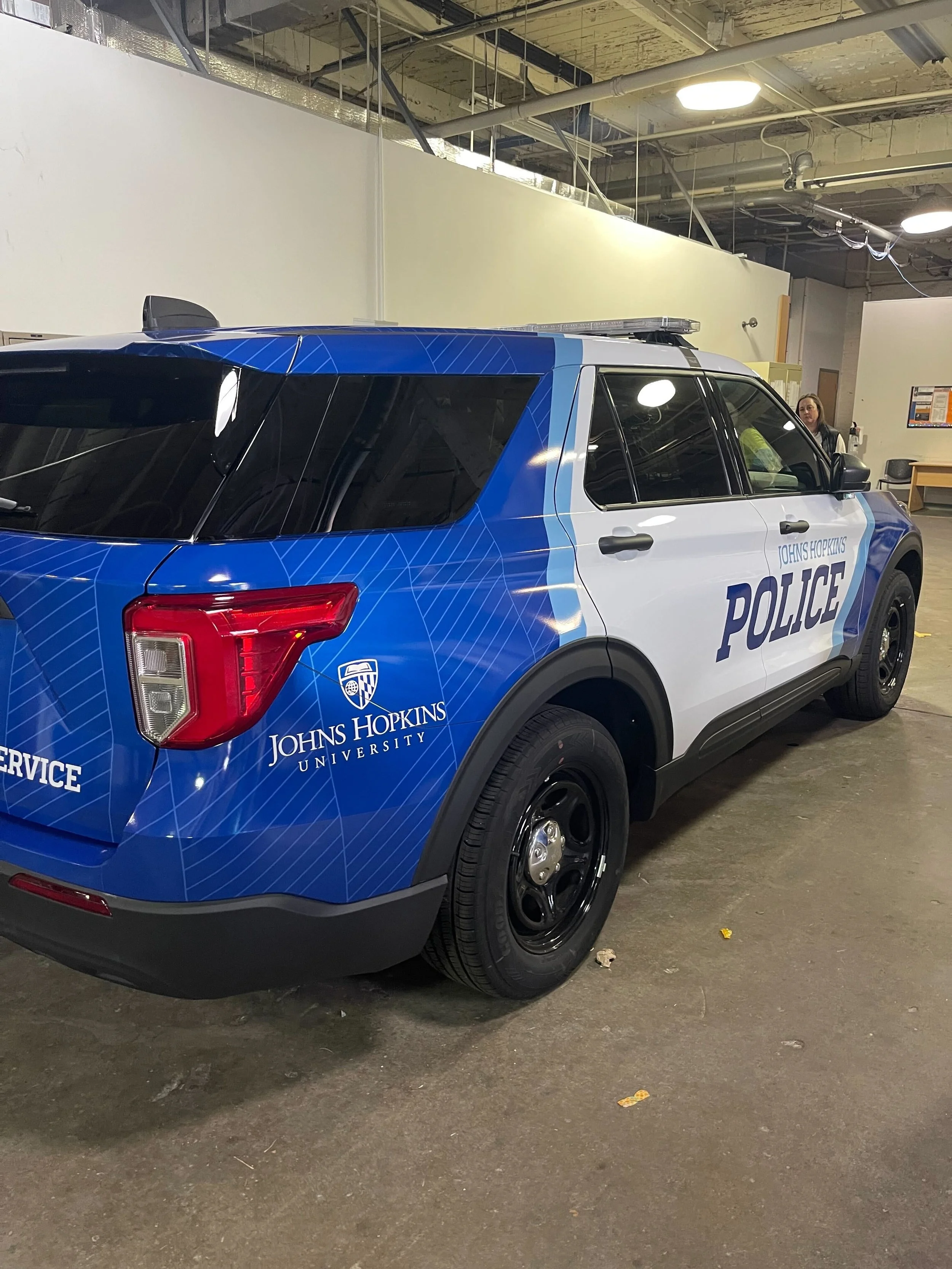 Johns Hopkins University police vehicle parked indoors, blue and white with university logo and 'POLICE' printed on the side.