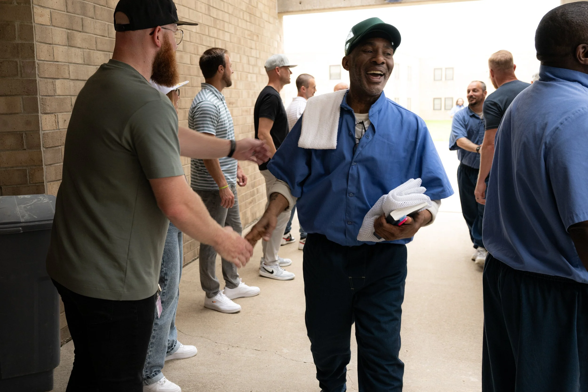 People shaking hands and engaging in conversation with inmates outside a building.