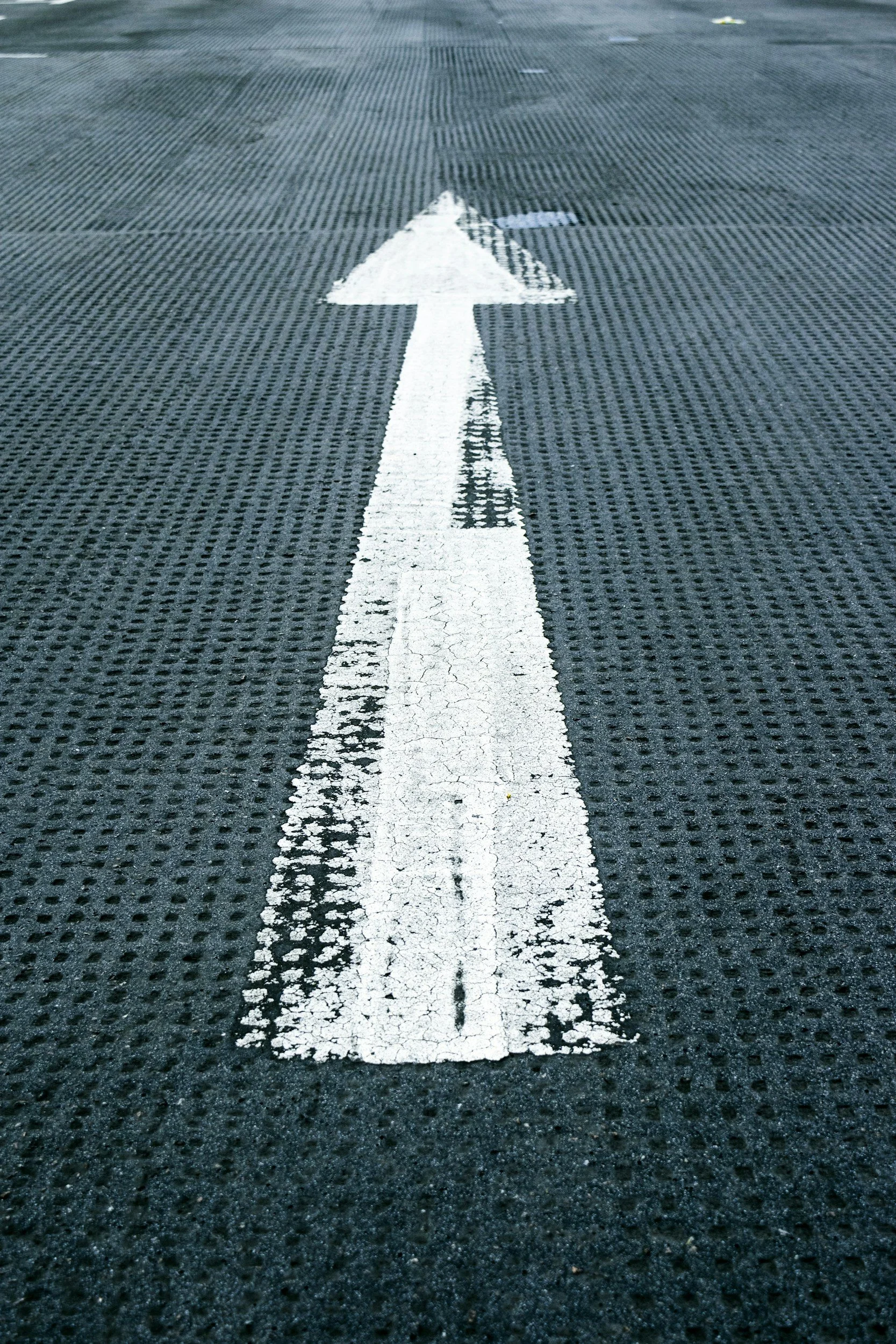White arrow painted on a textured asphalt road pointing forward.