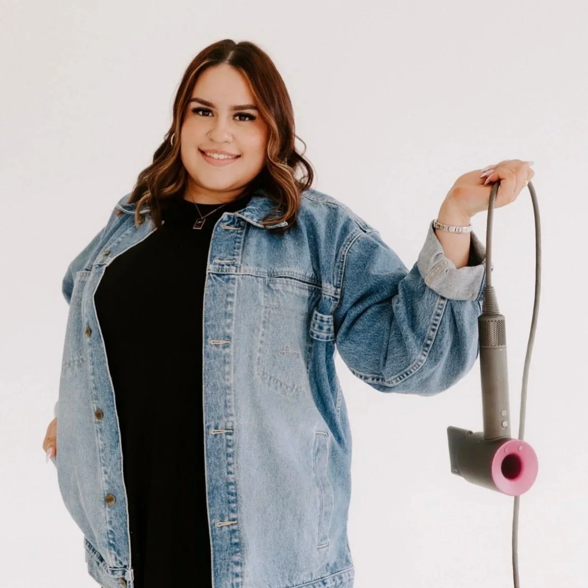 A young woman with brown hair, smiling, wearing a white t-shirt and a black-and-white gingham dress, standing against a black background.