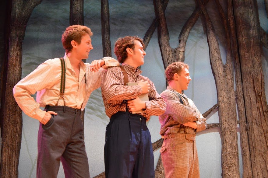 Three young men in period clothing stand on stage in front of a set resembling trees, appearing to be in a theatrical performance. Shenandoah John Anderson Totem Pole Playhouse