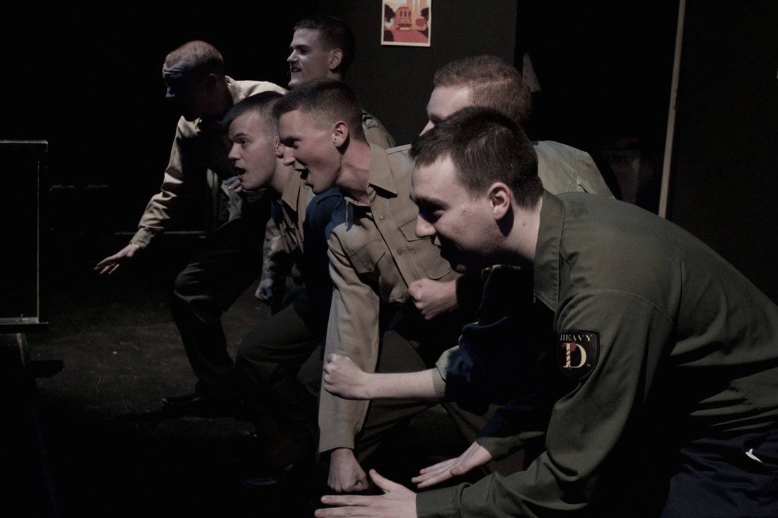 Group of young men dressed as military or police officers participating in a staged physical training or drill exercise in a dark room. Dogfight Boland Harvard