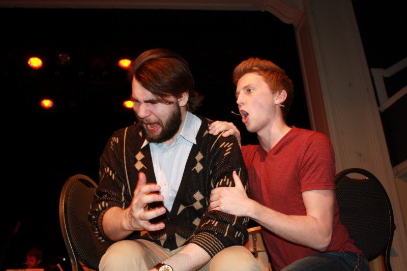 Two young men are sitting on chairs on a stage, with one comforting the other who appears distressed, under stage lighting. Next to Normal Gabe Berklee College of Music