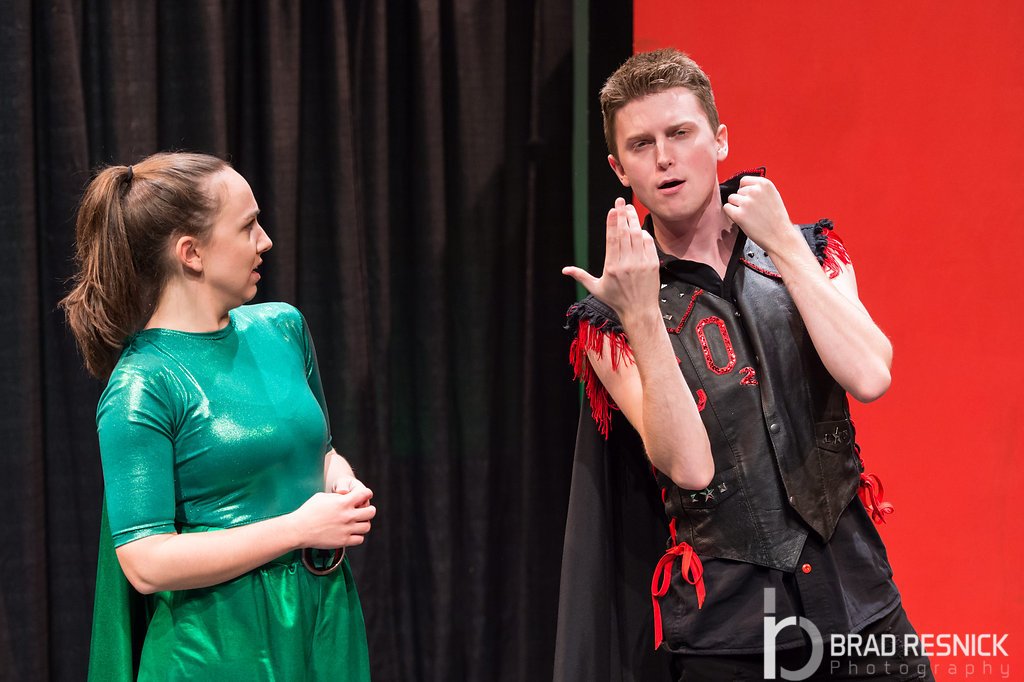 Two actors on stage in a theatrical performance, the man in a black vest with red fringe, in front of a black curtain and an orange background. Children's theater educational Gabi Goes Green George Street Playhouse.