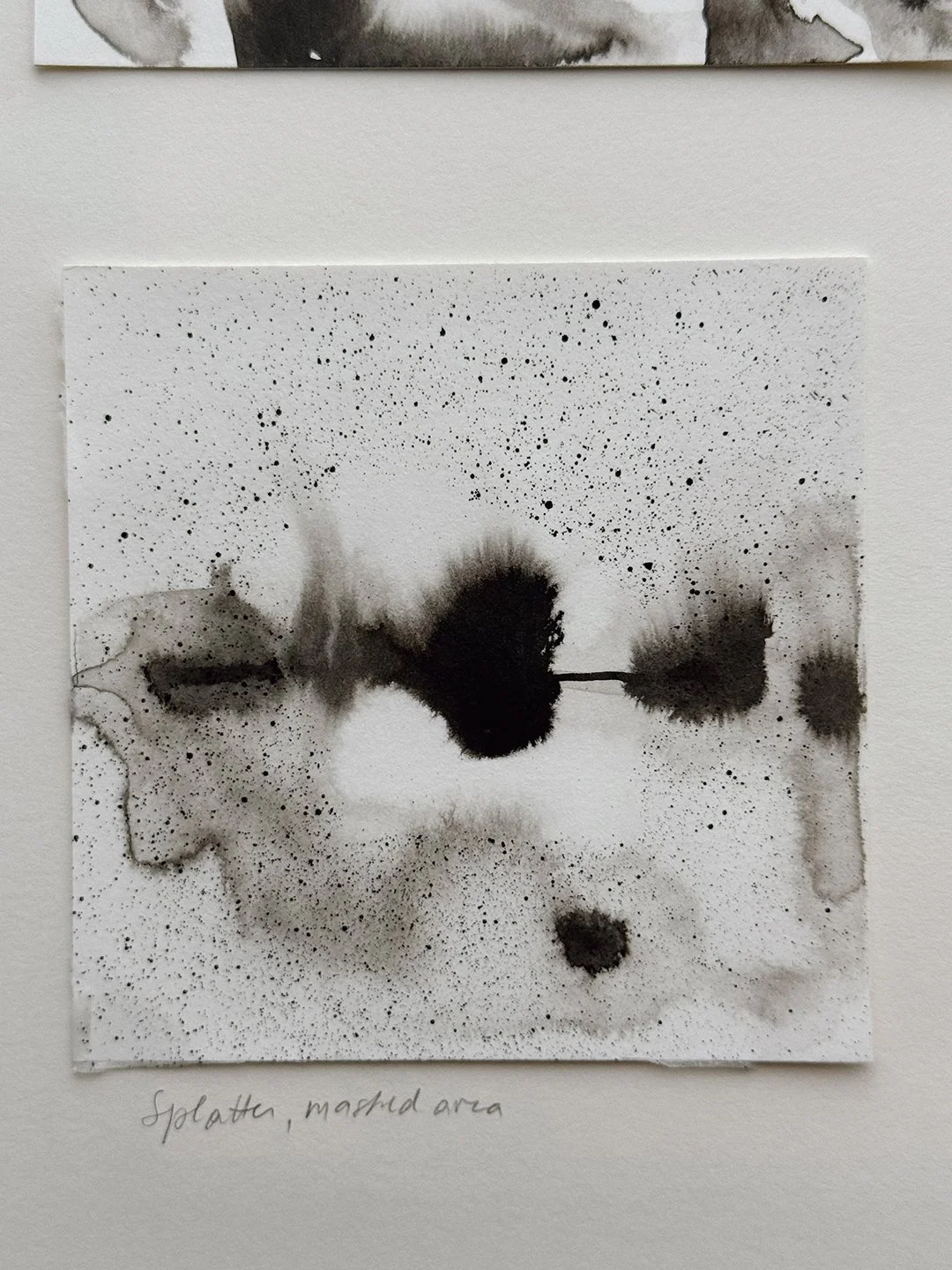 Ink study labelled "Splatter, masked area": fine black speckles across the paper around soft grey and black ink blooms that spread along a thin horizontal line.
