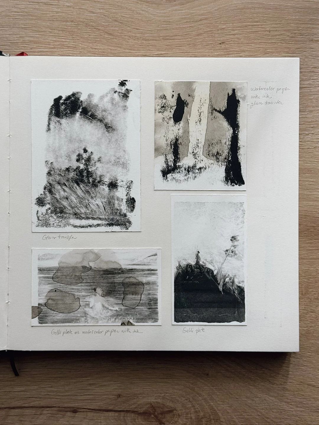 Sketchbook page with four black-and-white monotype tests: a glass transfer landscape, a glass transfer on inked watercolour paper, and two gelli plate prints.