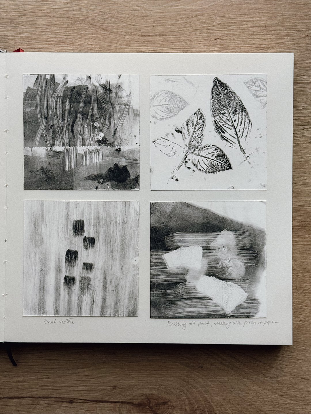 Sketchbook page with four square gelli plate monotypes: layered wavy lines, leaf prints, a brush-texture study, and brushed-off paint