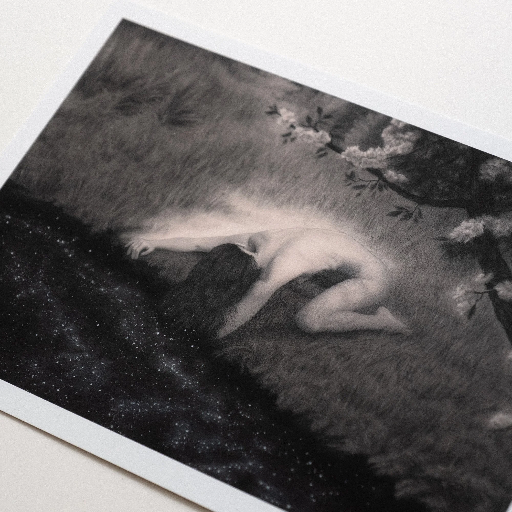 Graphite drawing of a kneeling woman beside dark water, her hair flowing into a star-filled river as she enters a moment of surrender and transformation.
