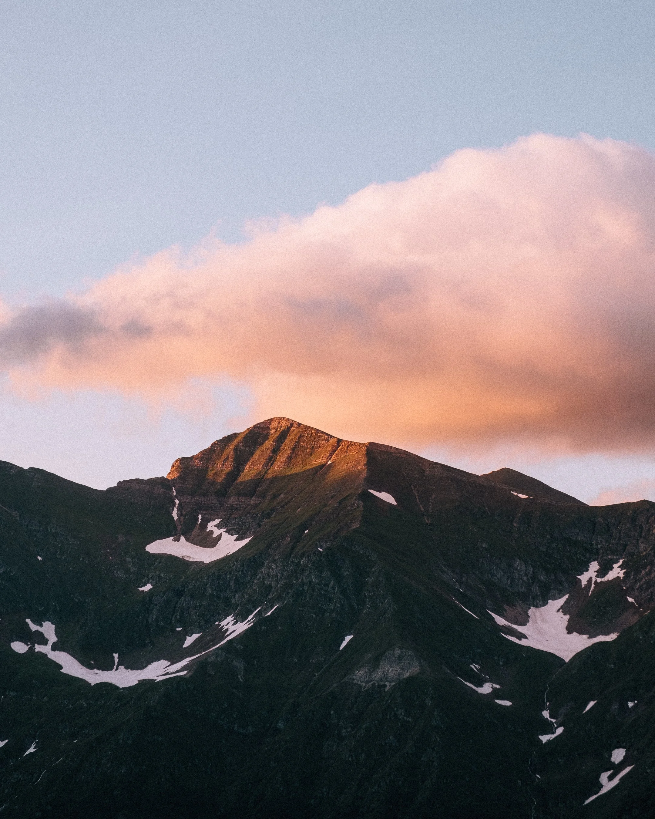 Sunset over a mountain with patches of snow, pink clouds in the sky