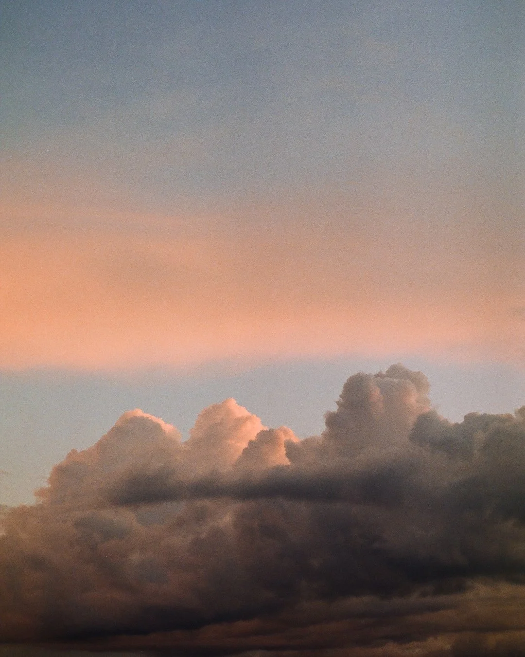 Sky with dark clouds near the bottom and light pink, orange, and gray clouds at sunset or sunrise