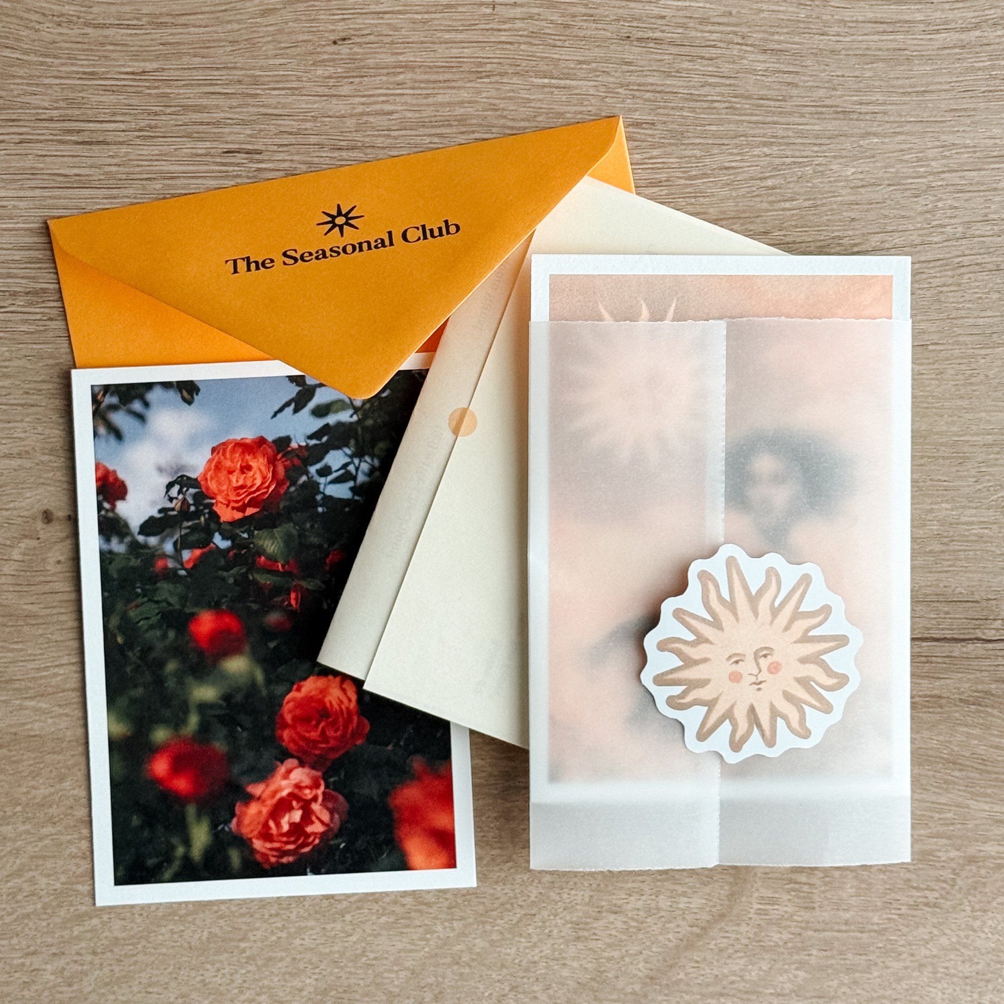 Flat lay of a yellow envelope, matching floral postcard, surreal art print and sticker on a wooden desk