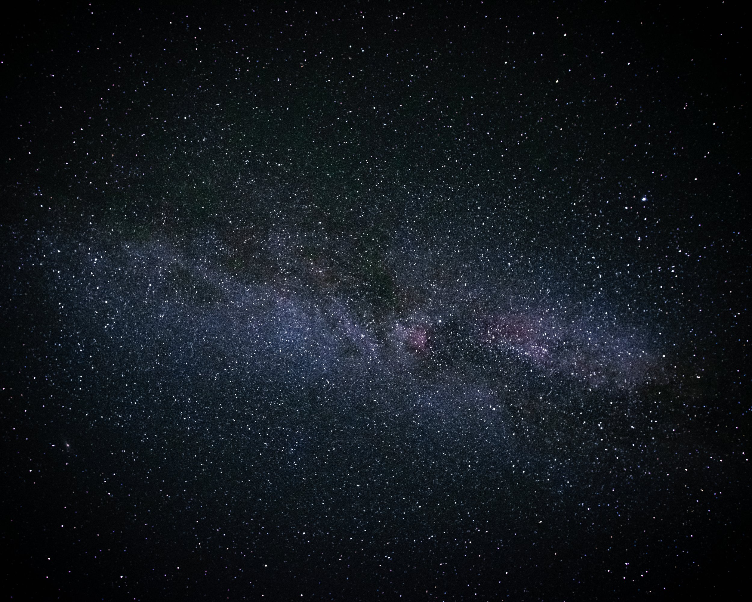 A clear night sky filled with countless stars and the faint glow of the Milky Way galaxy