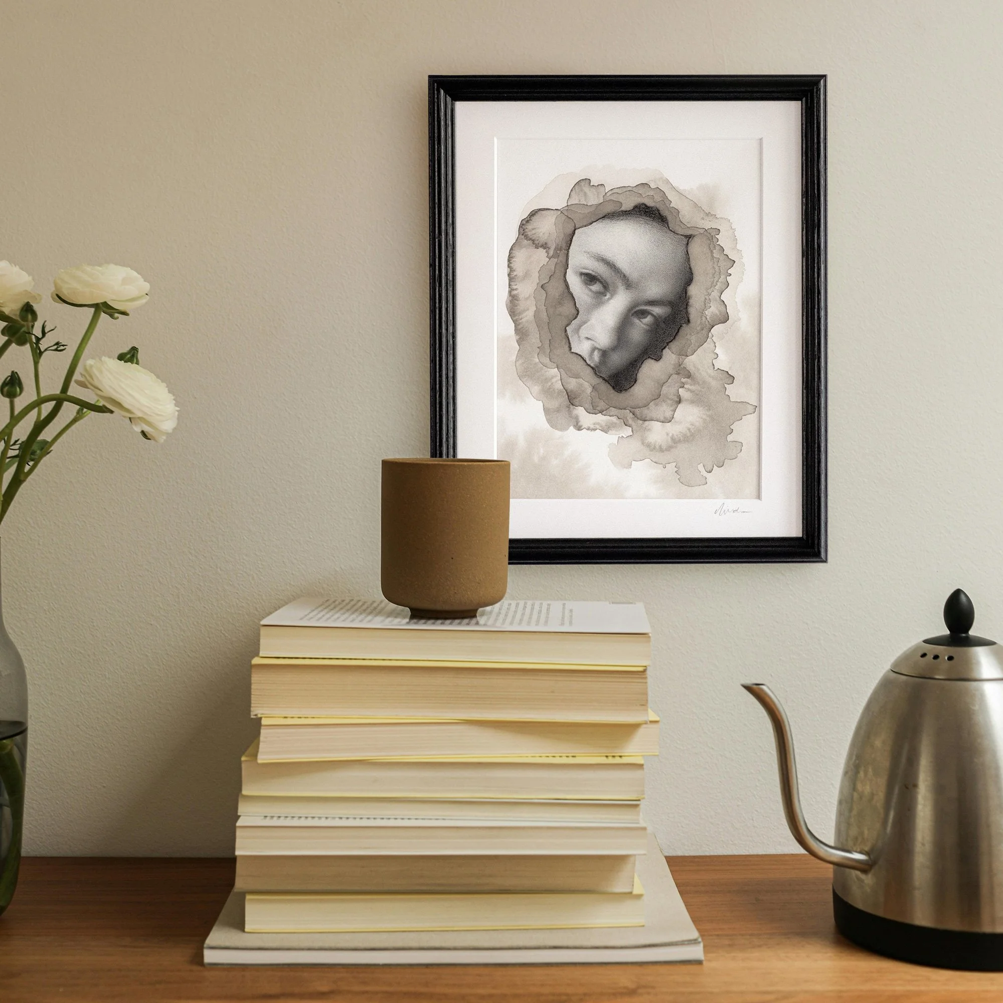 Original framed portrait drawing of a woman surrounded by abstract ink textures, placed on a wall next to books