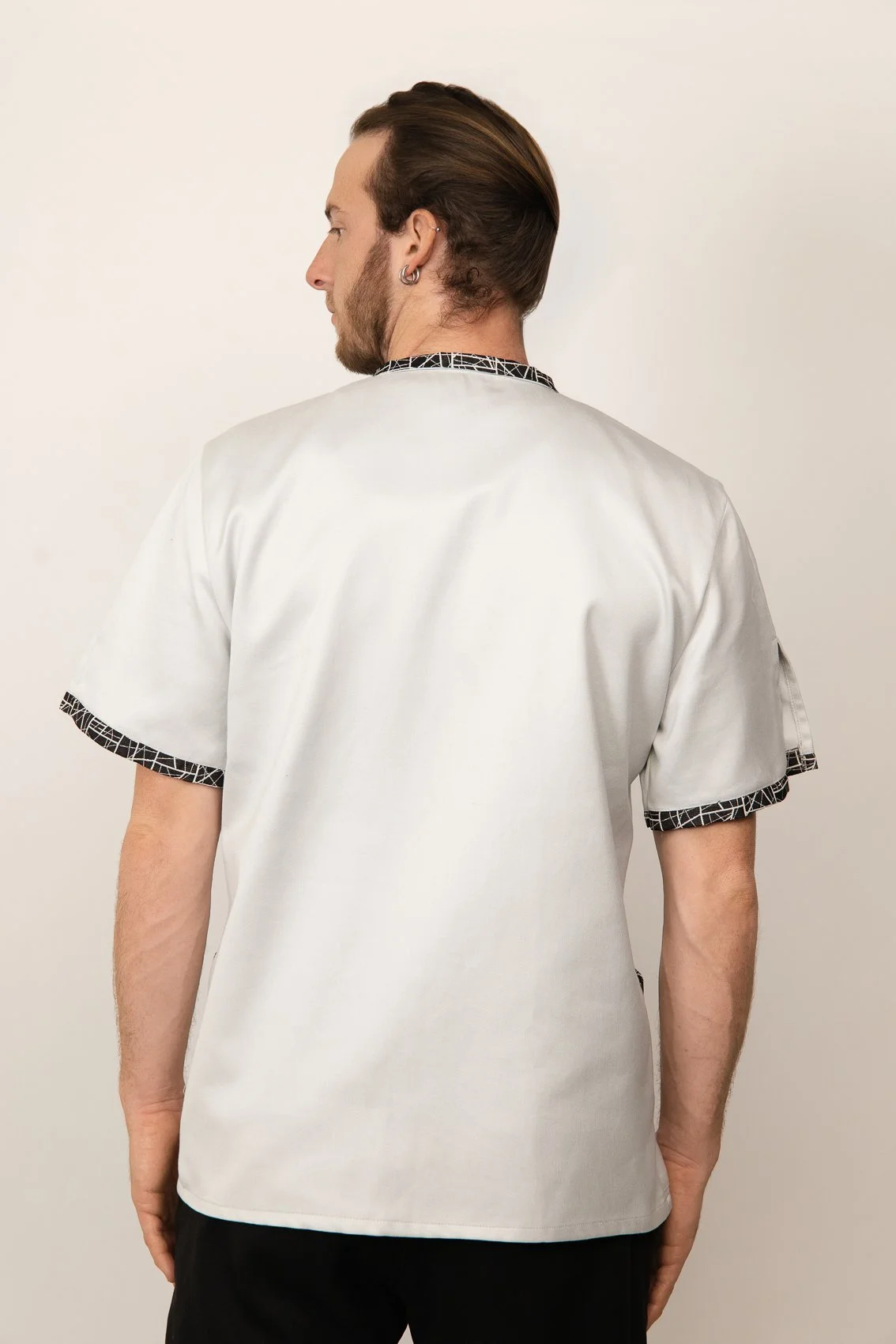 Un homme vu de dos portant une blouse médicale blanche avec des détails noirs et blancs aux manches et au col.