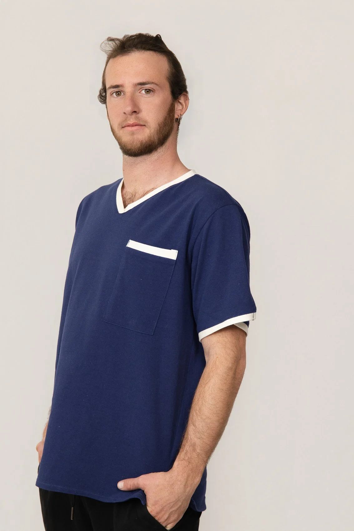 Homme portant un t-shirt médicale bleu avec des bordures blanches, posant contre un fond blanc.