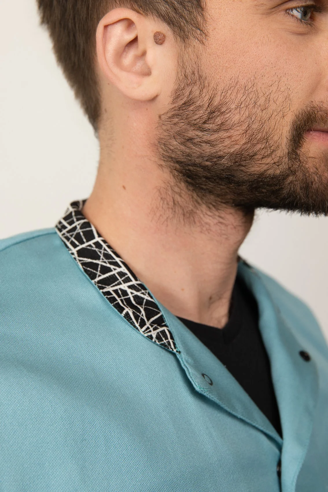 Un homme vêtu d'un blouse médicale bleue avec un col à motif noir et blanc.