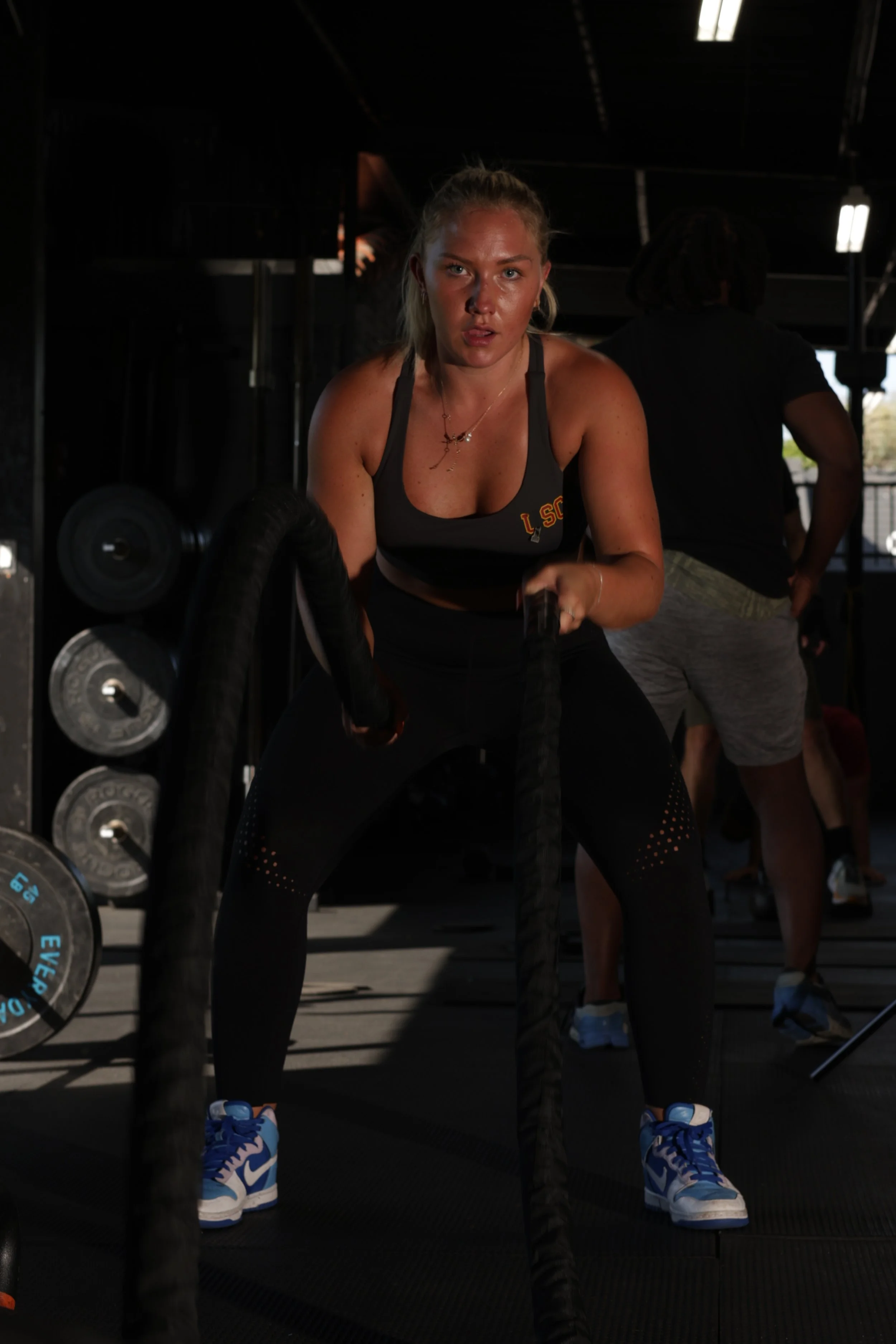 A woman in workout clothes using battle ropes in a gym.
