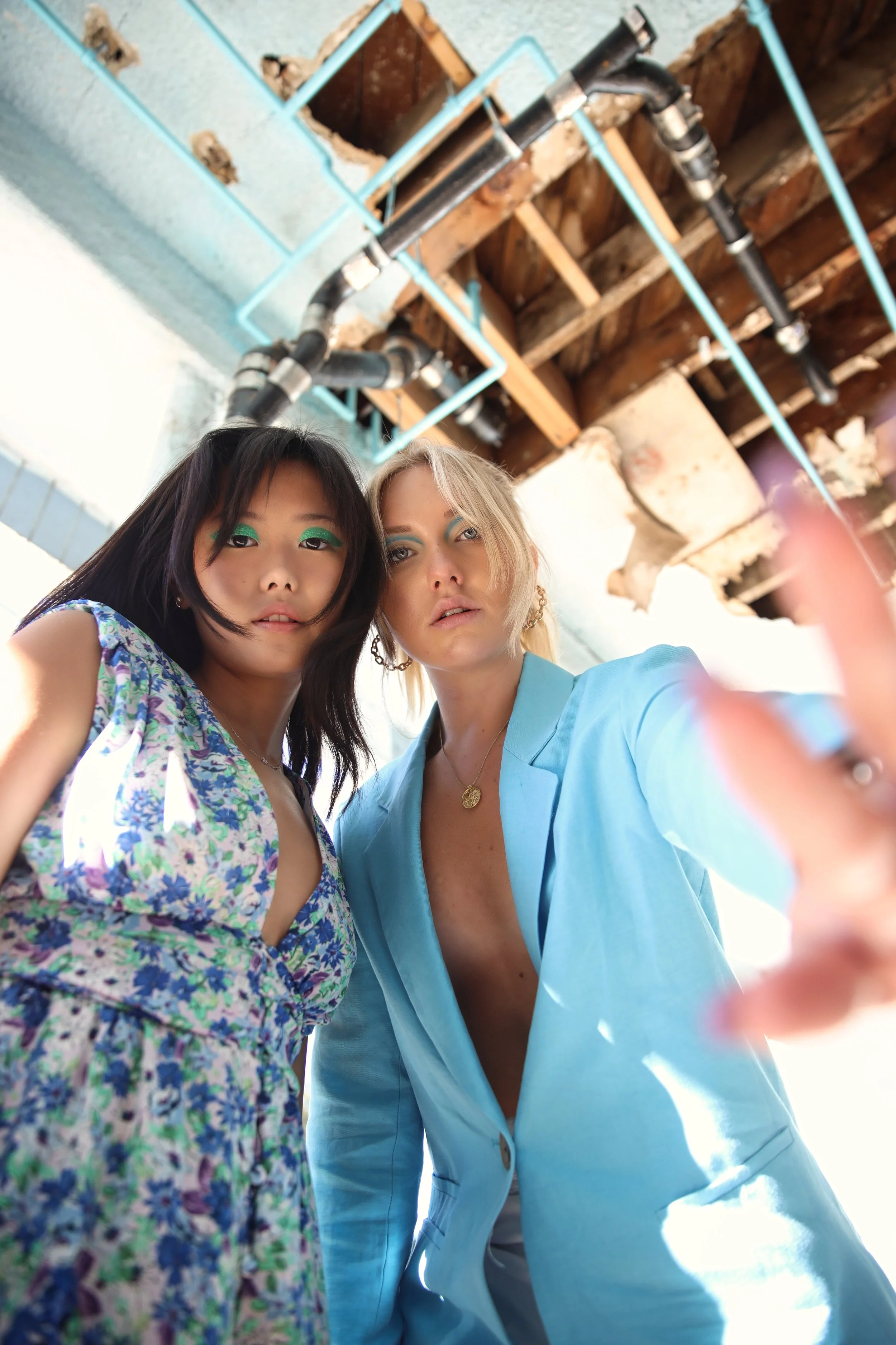 Two women taking a selfie at a construction site with exposed pipes and wooden beams in the background.