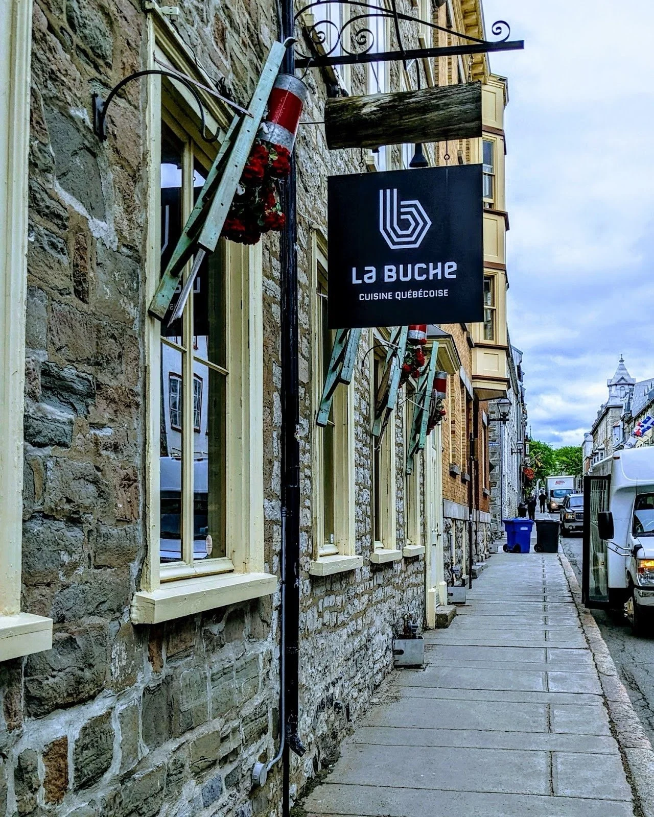 Façade d'un restaurant québécois nommé La Bûche avec un panneau noir, fenêtres à cadre beige, décorations de Noël et un trottoir en ville.