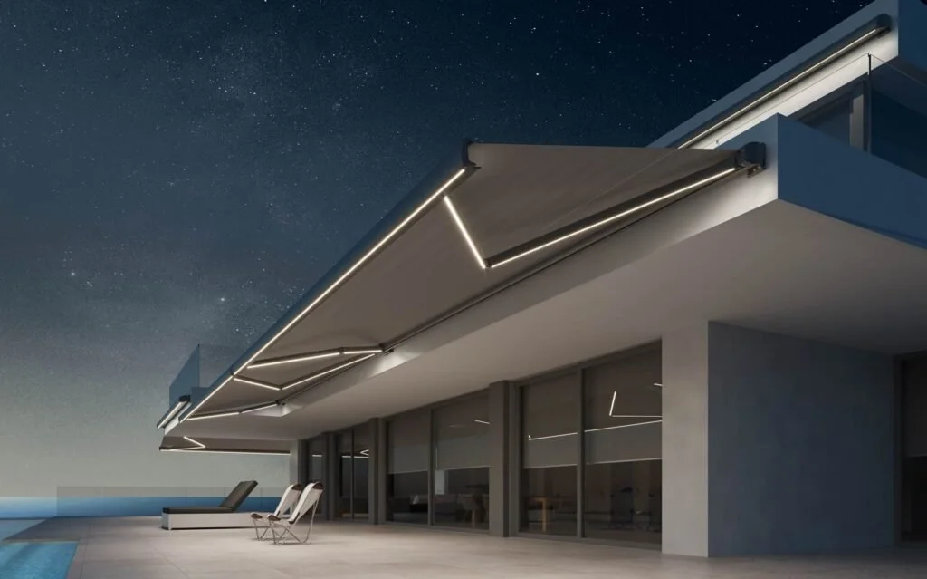 Image of an outdoor awning with LED lighting on the extension arms extending above a pool patio on a modern home.