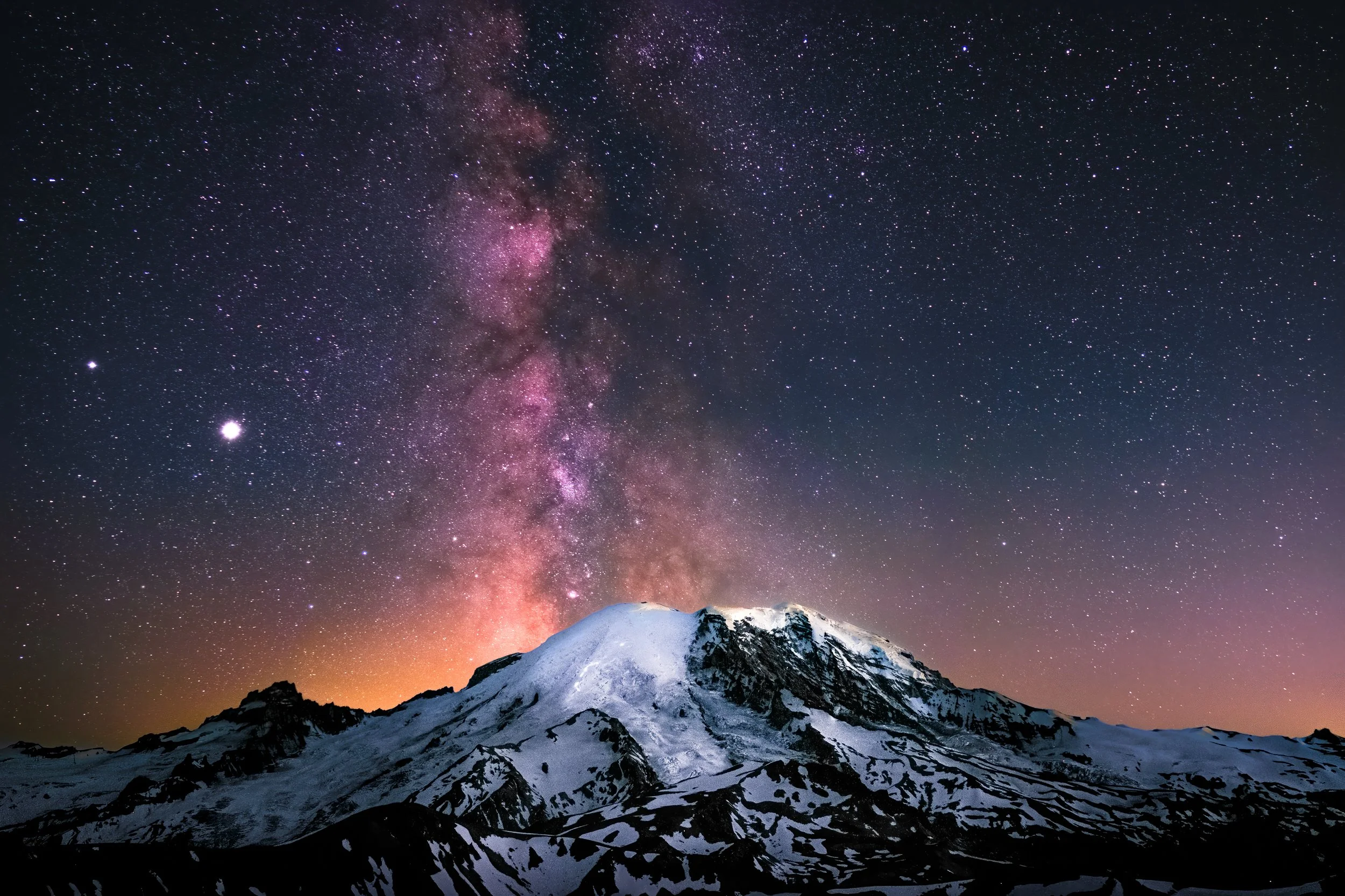 Snow-capped mountain at night with a star-filled sky and the Milky Way galaxy overhead.