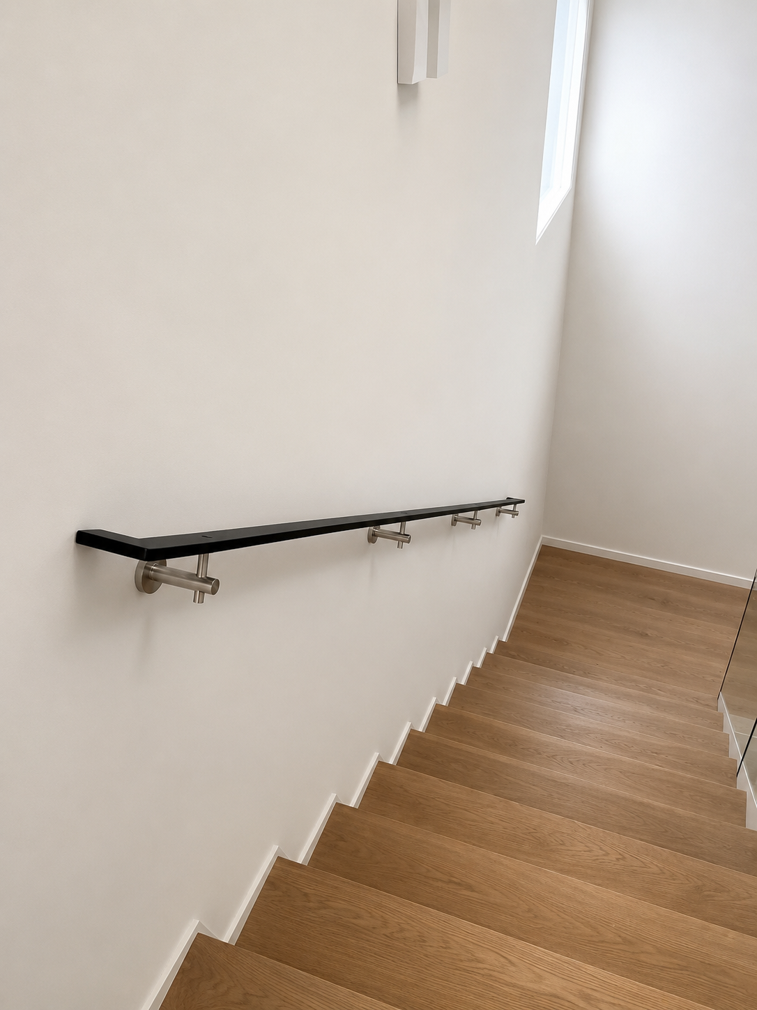 Wooden staircase with white wall and metal handrail, window in the corner letting in natural light