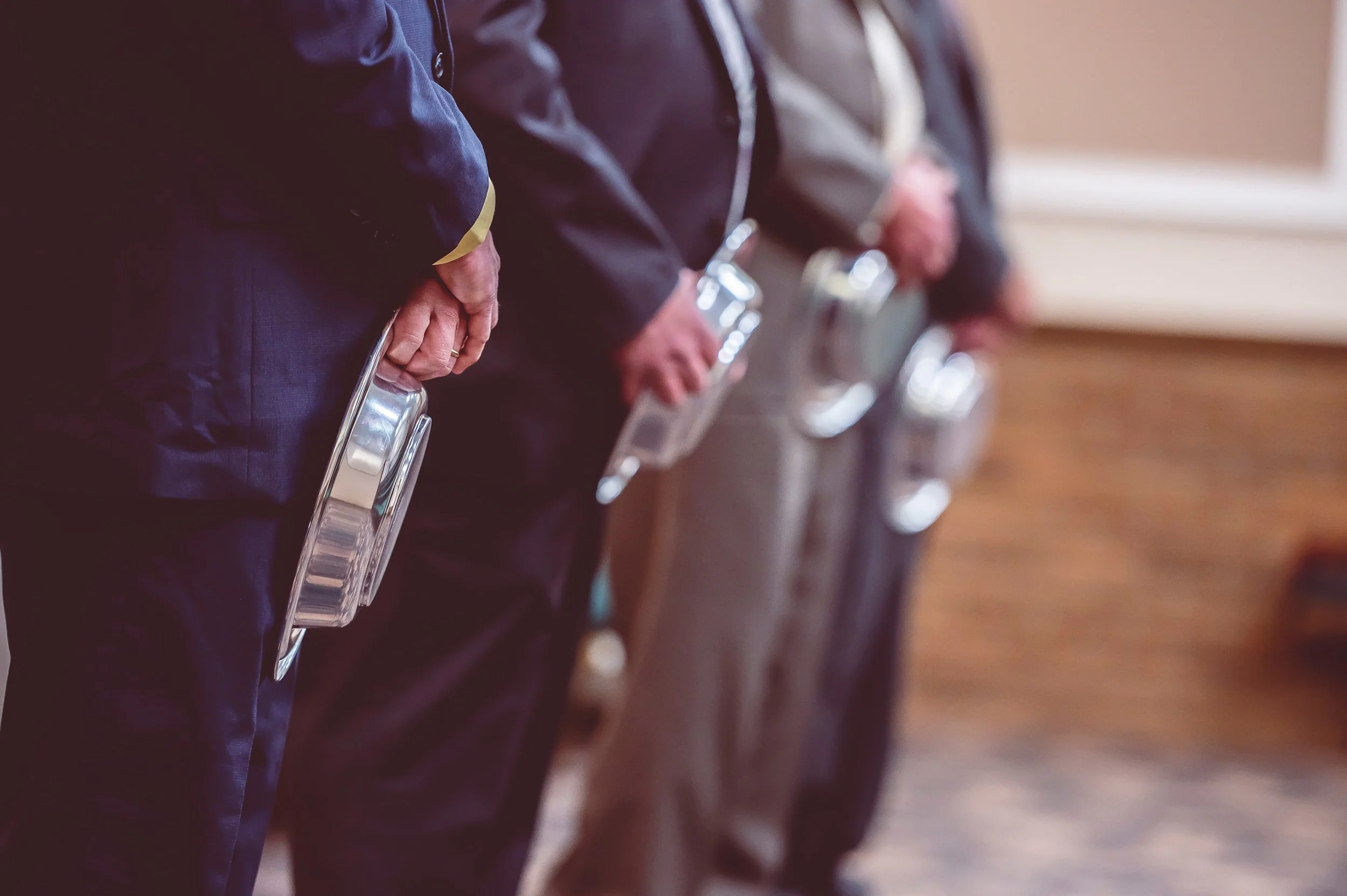 A line of people standing close together, each holding a clear plastic container, in an indoor setting with a wooden wall.