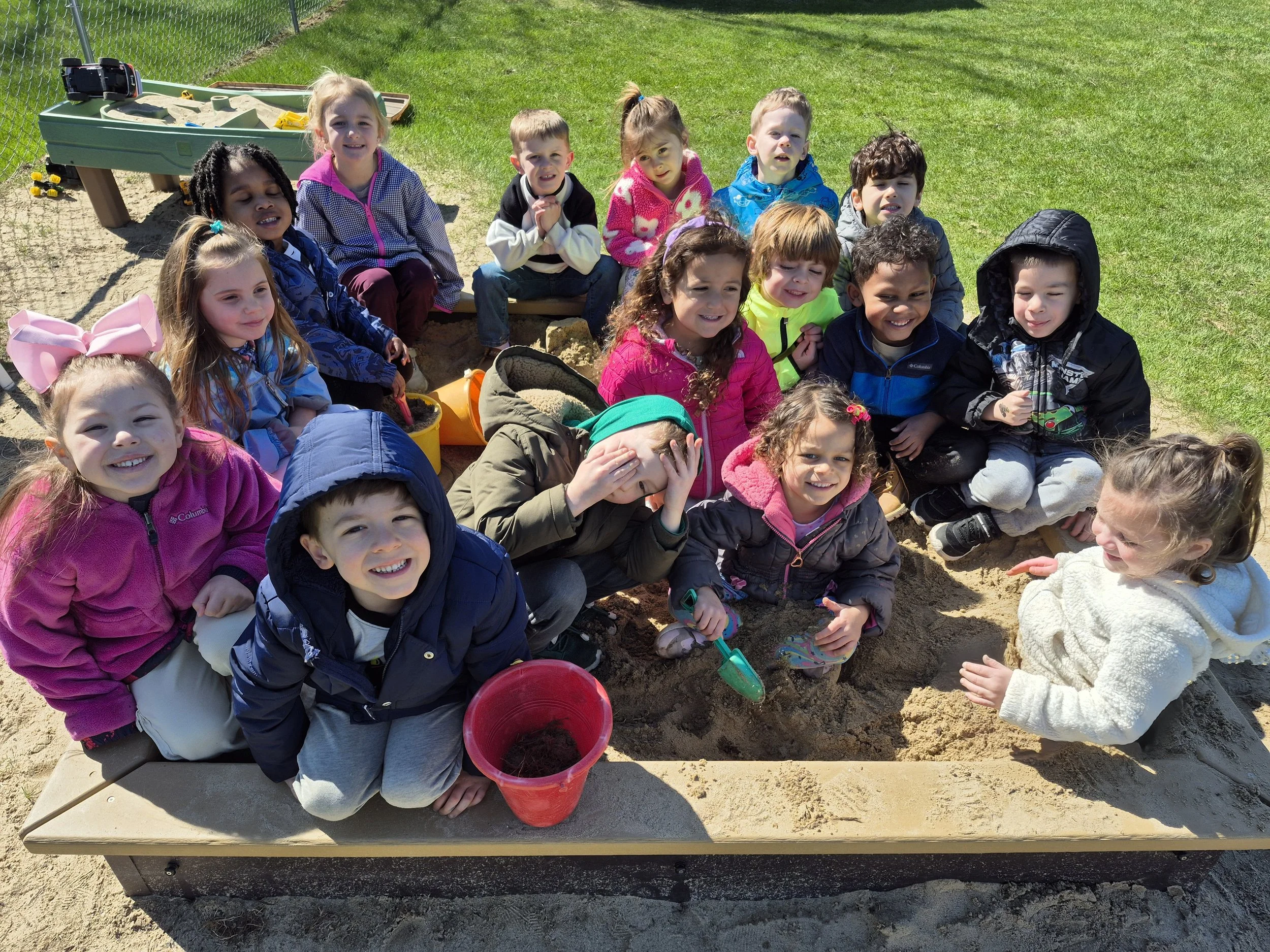 Group of children playing in a sandbox at a playground on a sunny day.