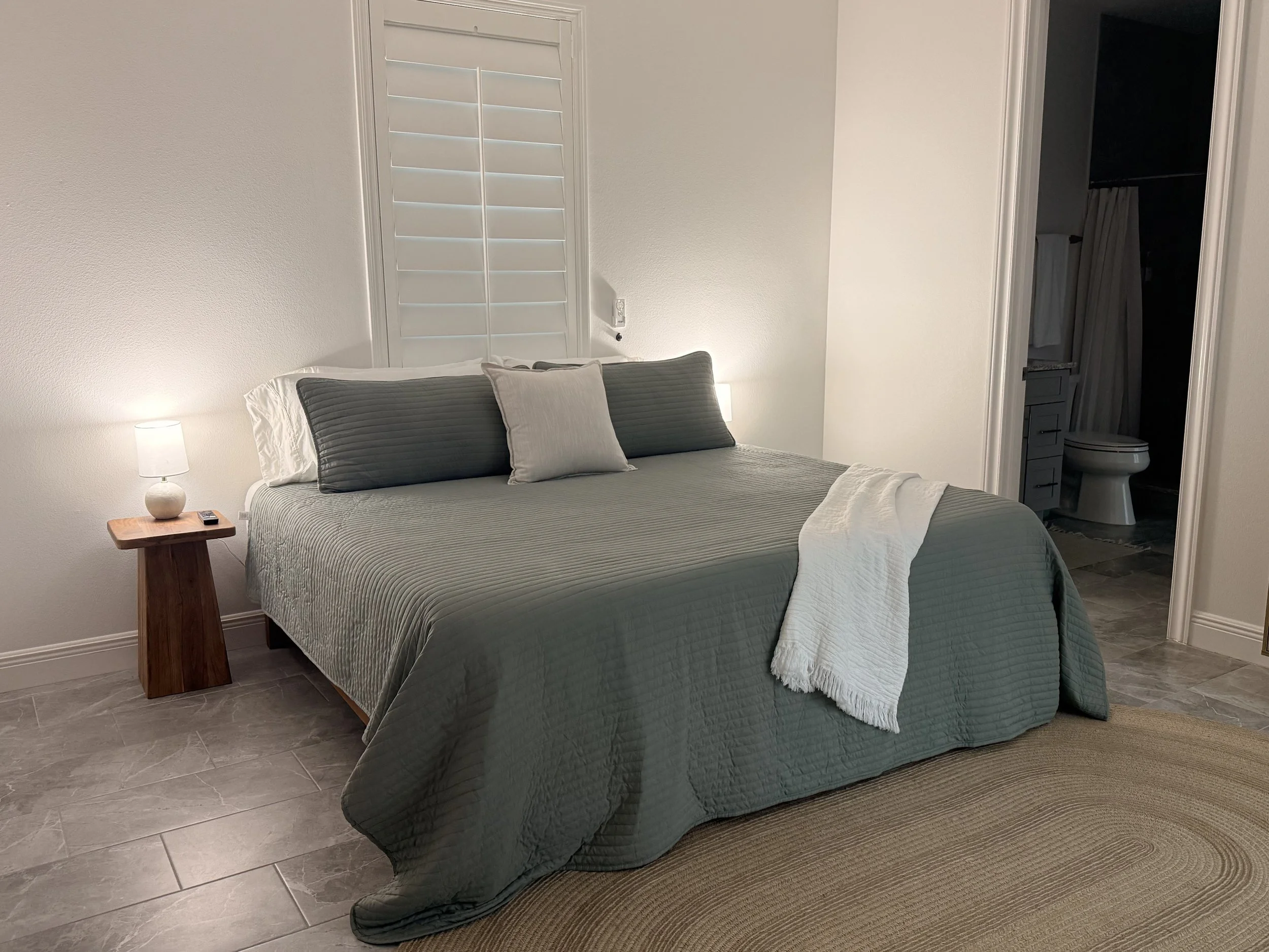 Modern office lounge area with white, green, and black chairs, a large black floor lamp, a gray sofa, and large windows letting in natural light, with wooden wall decor and glass partition.