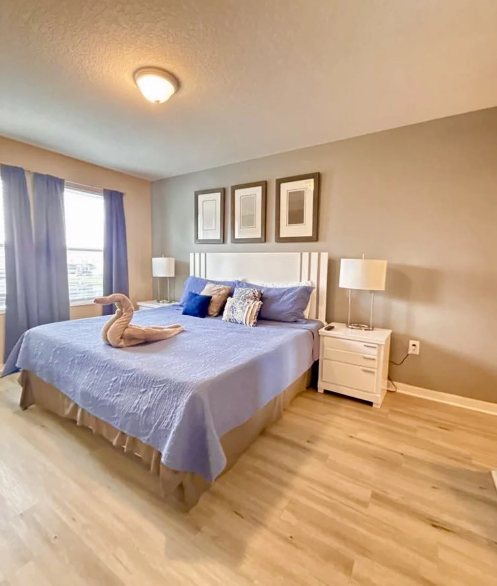 Modern white kitchen with large island, six white and gold chairs, pendant lights, white cabinets, and sliding glass doors to backyard.