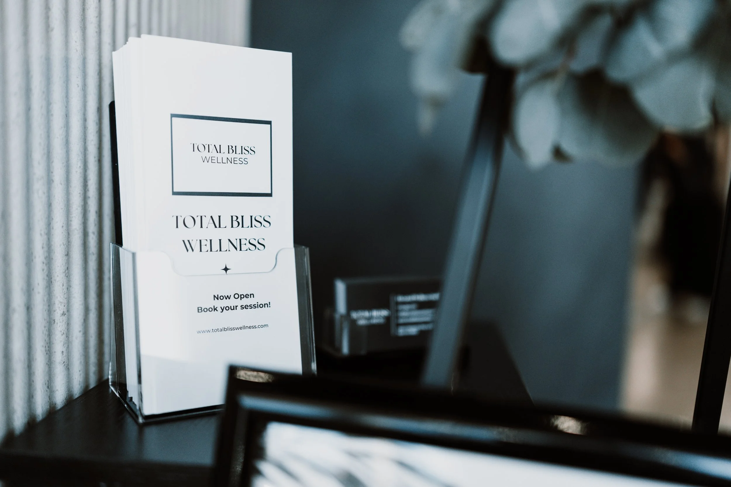 Modern living room with open sliding doors to a patio offering views of a desert landscape. Indoor has a ceiling fan, wooden dining table set, beige sofa, and stylish decor. Outdoor has cushioned seating and a small wooden table.