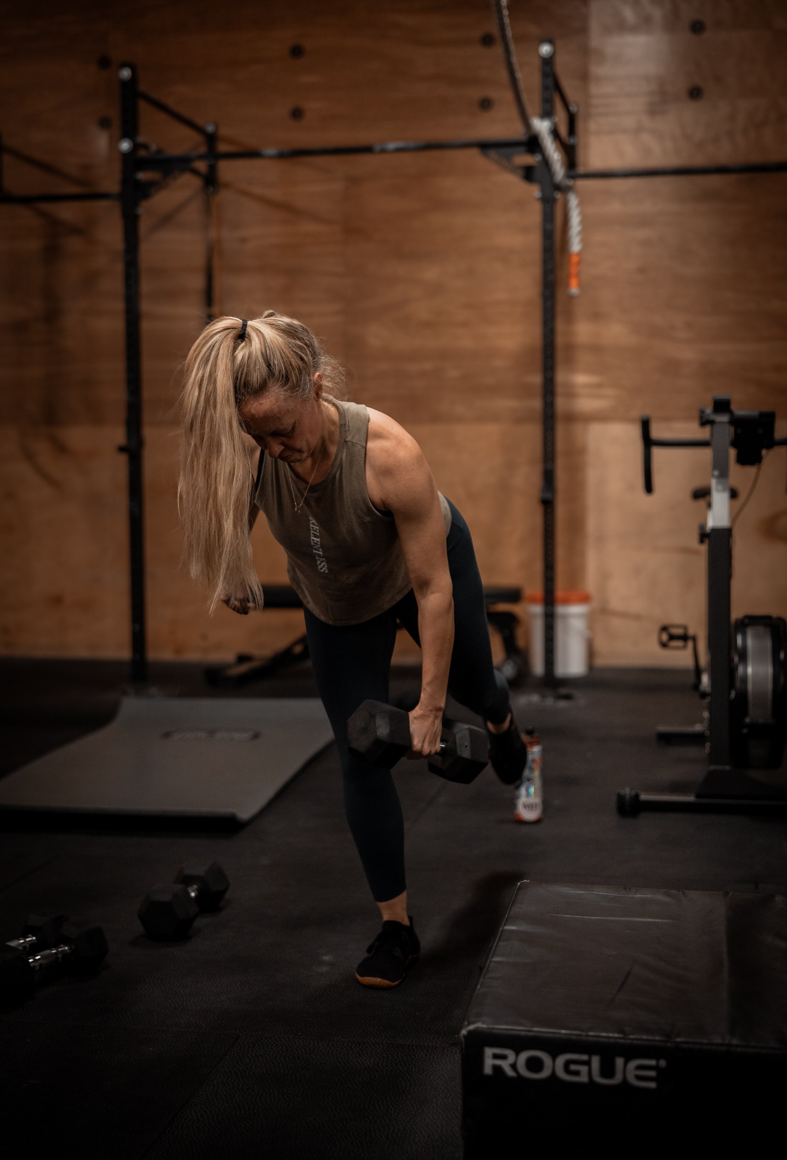 A woman performing a single-leg deadlift with dumbbells in a gym.