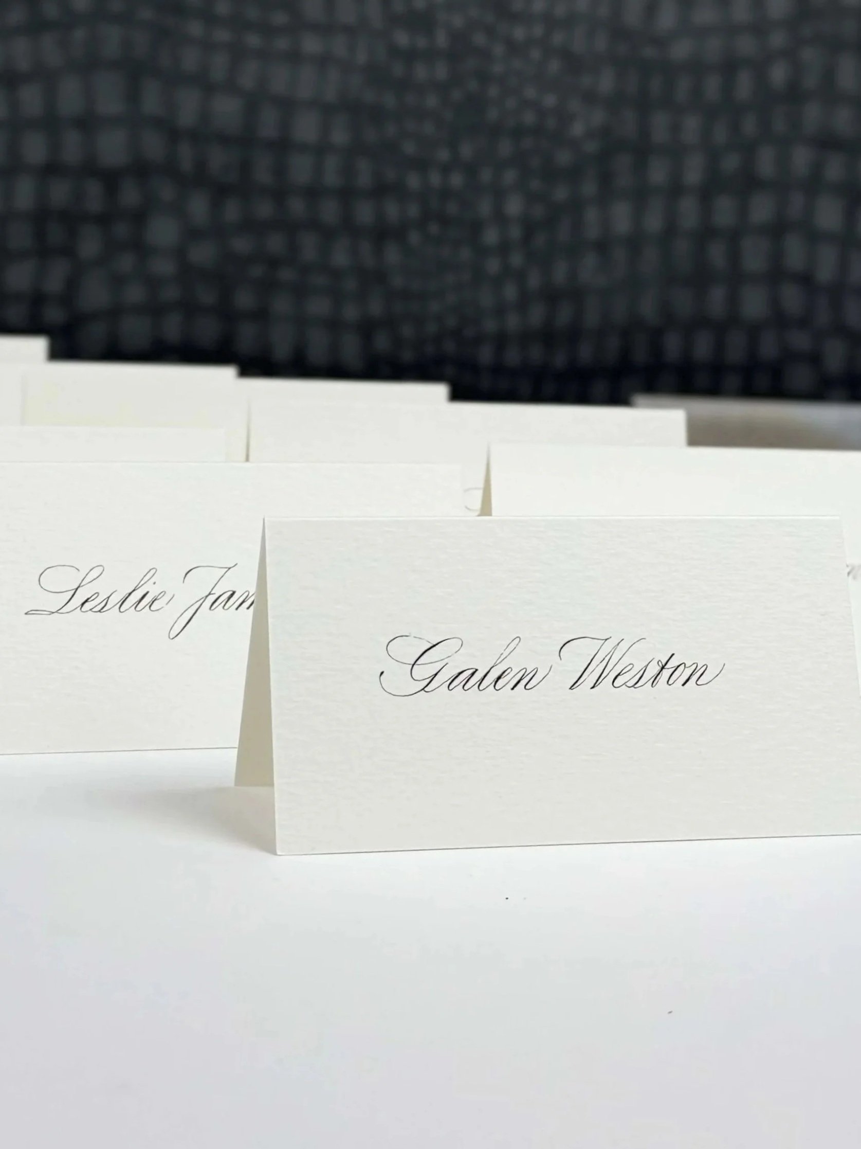 Place cards with names written in copperplate script with a dark, textured background.