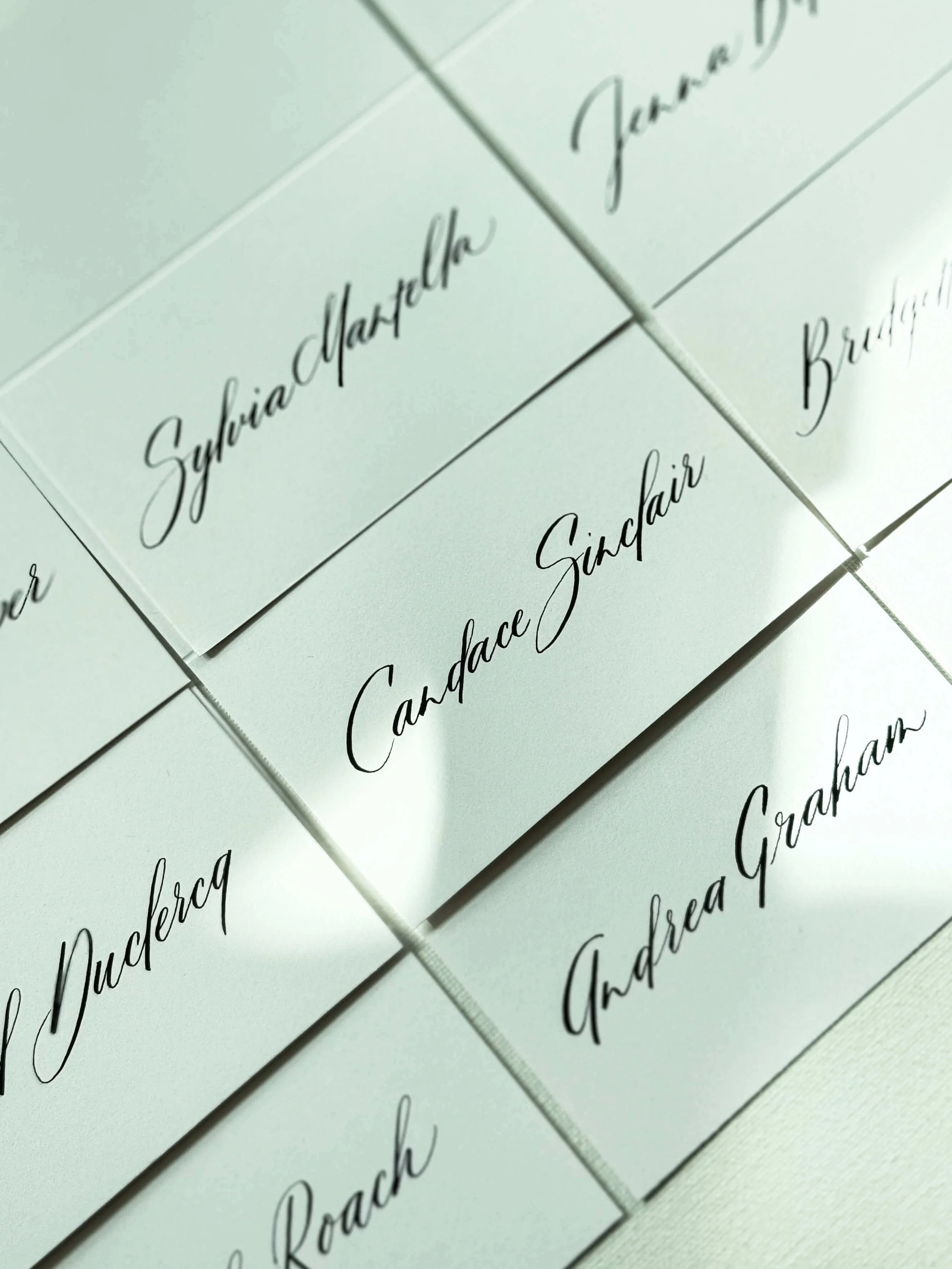 Close-up of white cards with black cursive writing, featuring names like Canada Sinclair, Sylvia Manchester, and Andrea Graham.