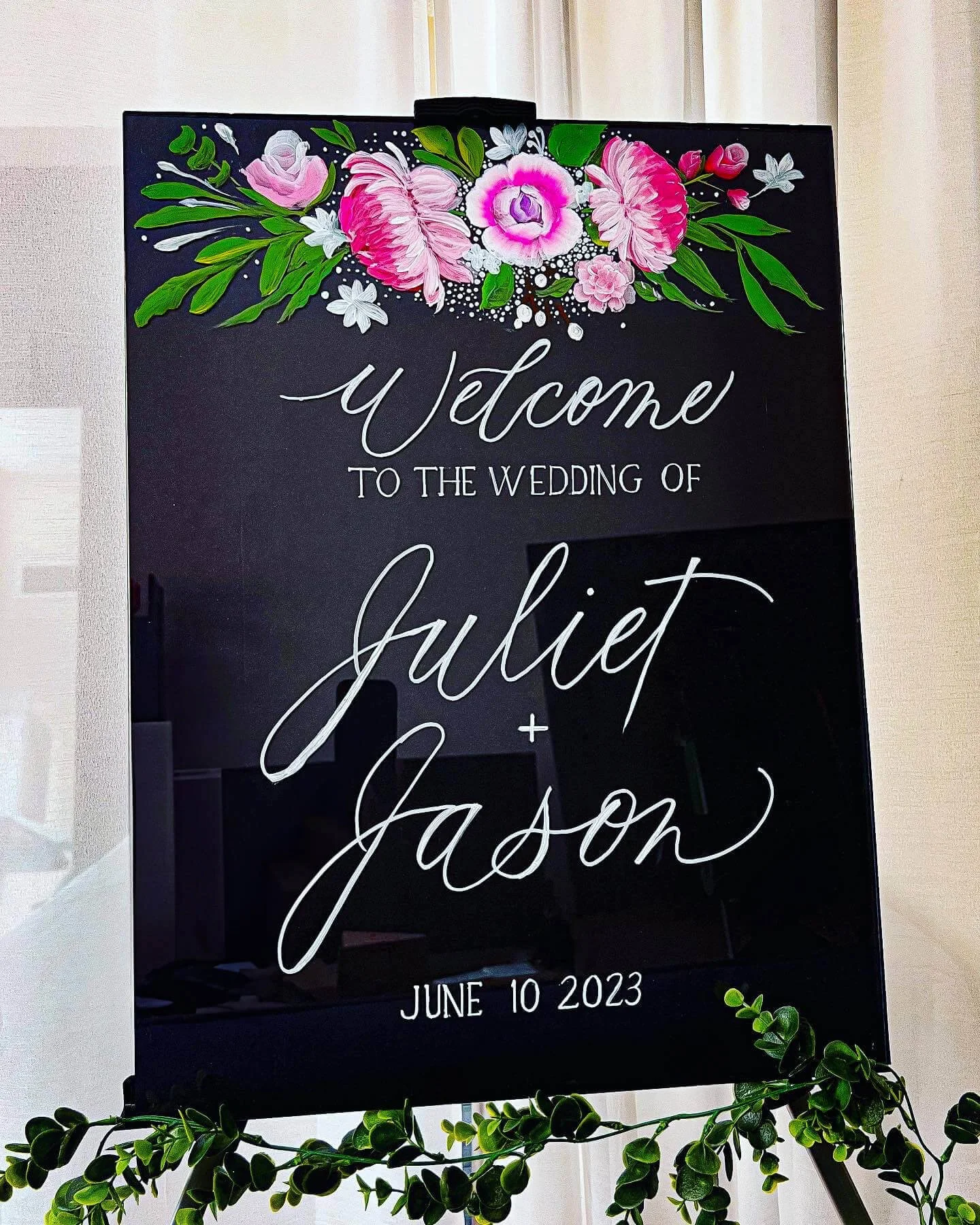 Wedding welcome sign with floral decorations, displaying the names Juliet and Jason in modern brush calligraphy, and the date June 10, 2023.