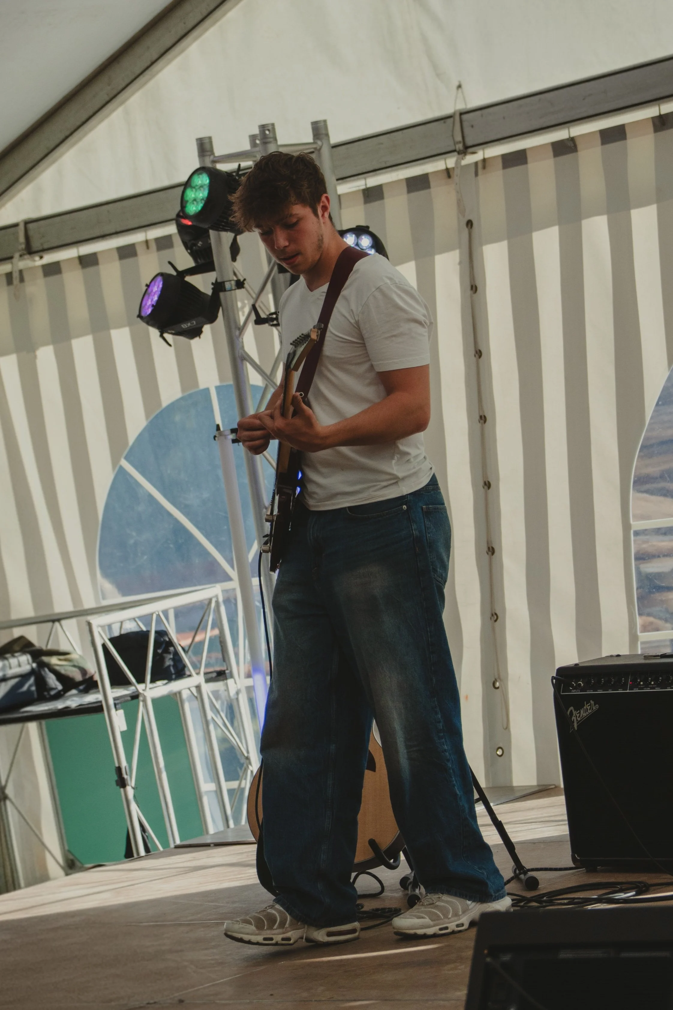 Junger Mann spielt Gitarre auf einer Bühne in einem Festzelt, mit mehreren Scheinwerfern im Hintergrund.