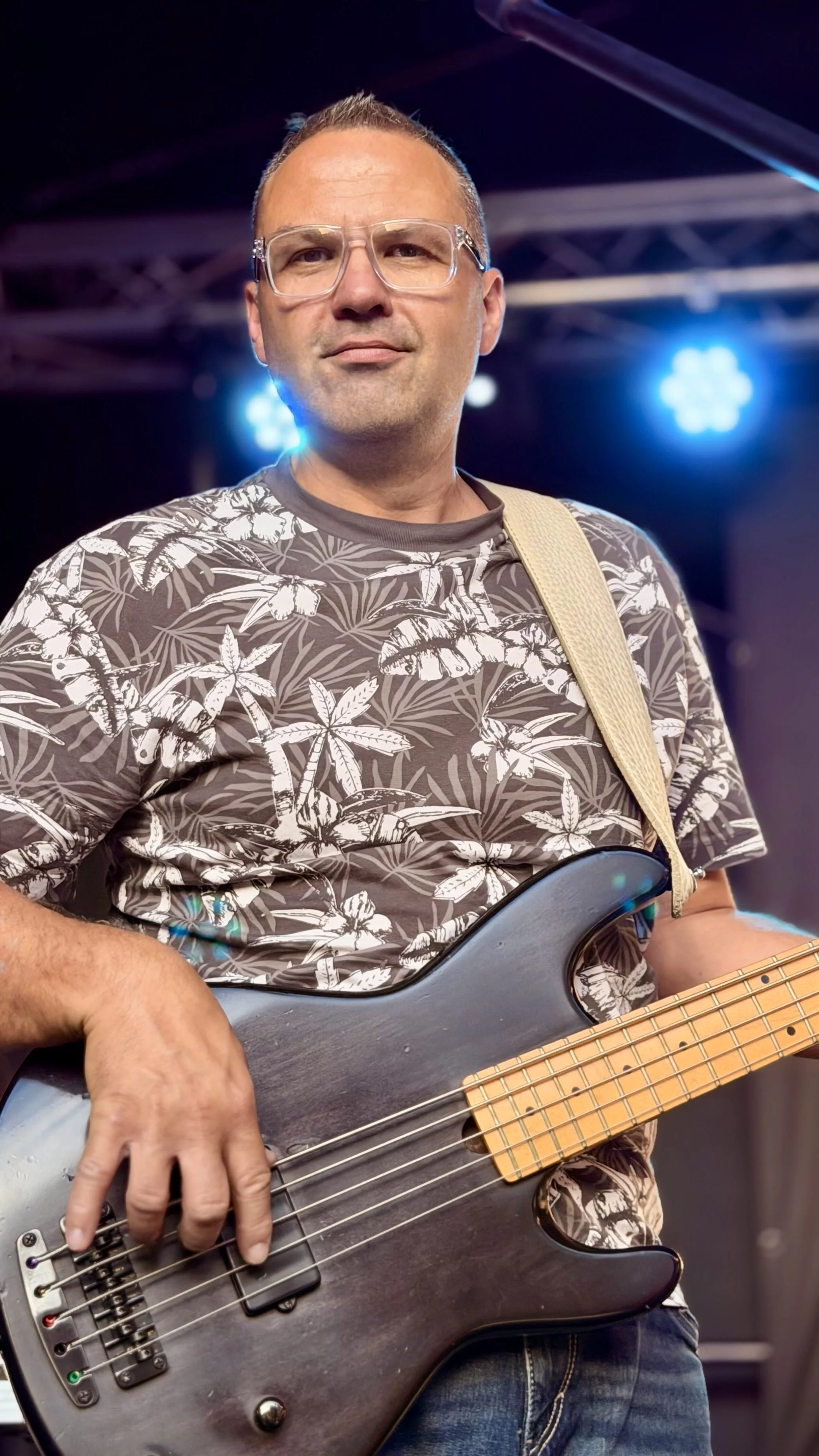 Ein Mann spielt E-Bass auf einer Bühne mit blauen Lichtern im Hintergrund.