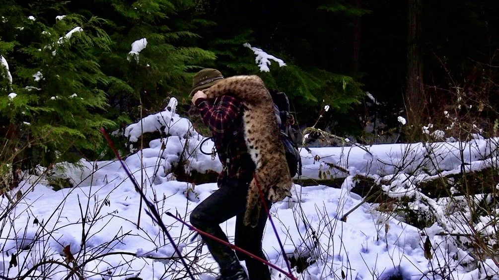 A person in winter outdoor gear walking through a snowy forest while carrying a mountain lion on their shoulders.