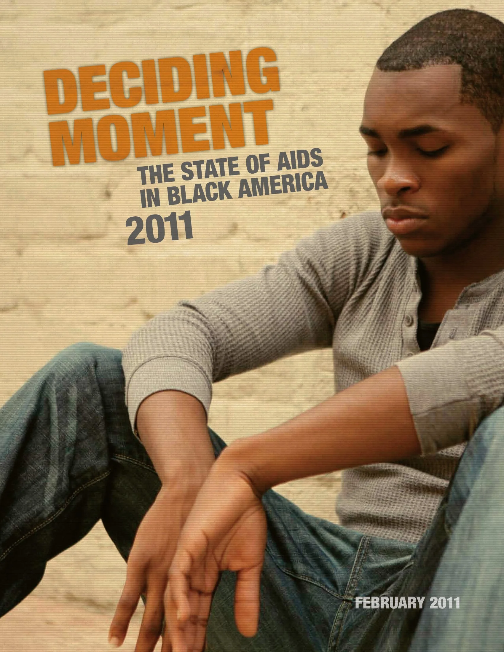 Black man in grey top and blue jeans slouched on the ground leaning on a wall looking down