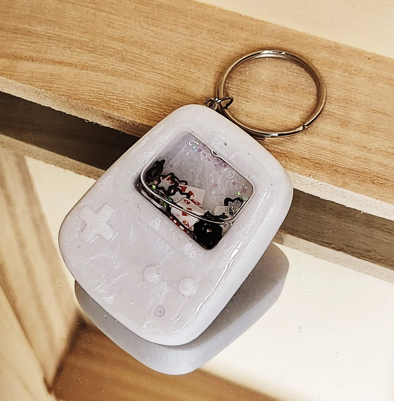 Poker player wet shaker keychain
White resin handheld game with clear resin sealer top, filled with glitter, foam playing cards, foam poker chips, and stars (inner liquid is baby oil)