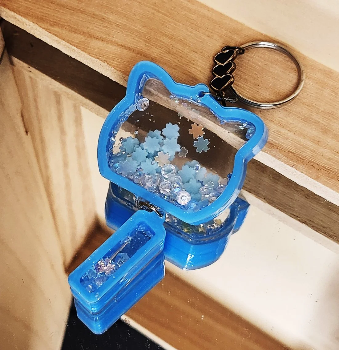 Celebration cat dry shaker keychain
Clear resin with blue edges in the shape of a cat head plus a tassel, filled with glitter, rhinestones, and glow-in-the-dark foam snowflakes
