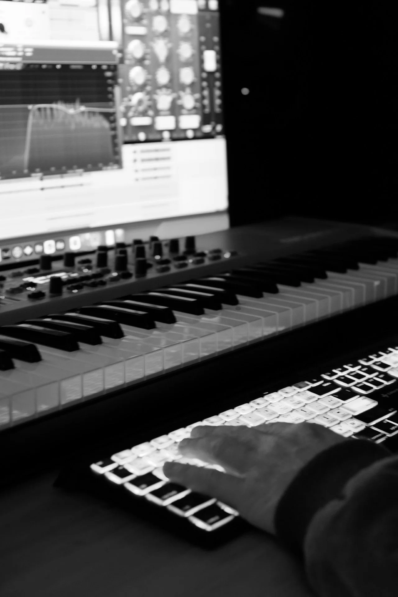 Ein Klavierspieler nutzt ein MIDI-Controller mit beleuchteten Tasten, vor einem Laptop mit Musiksoftware. Der Bildschirm zeigt ein DAW-Programm mit einer Wellenform und mehreren Spuren.