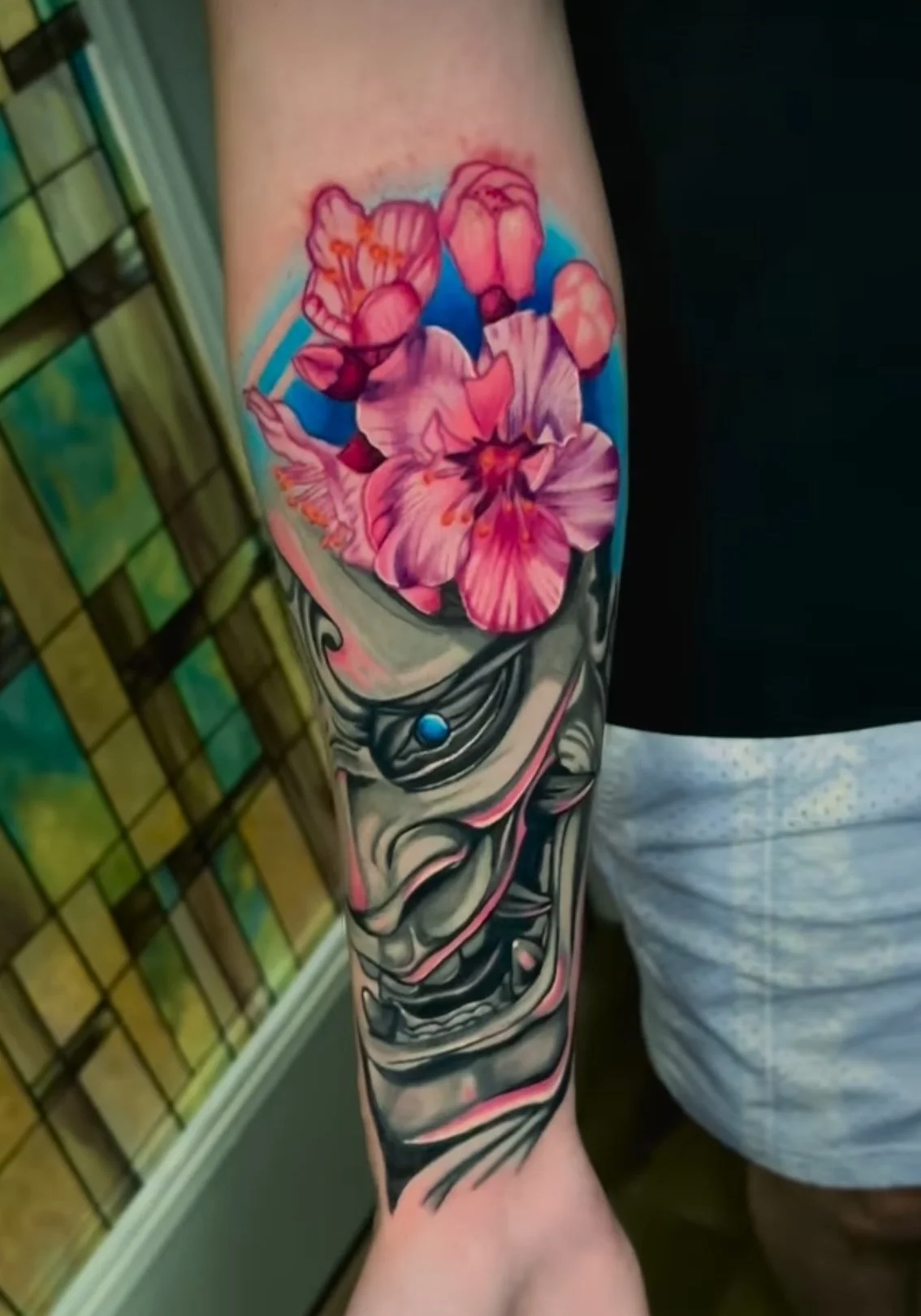 Tattoo of a clown face with a bouquet of pink flowers on the upper arm.