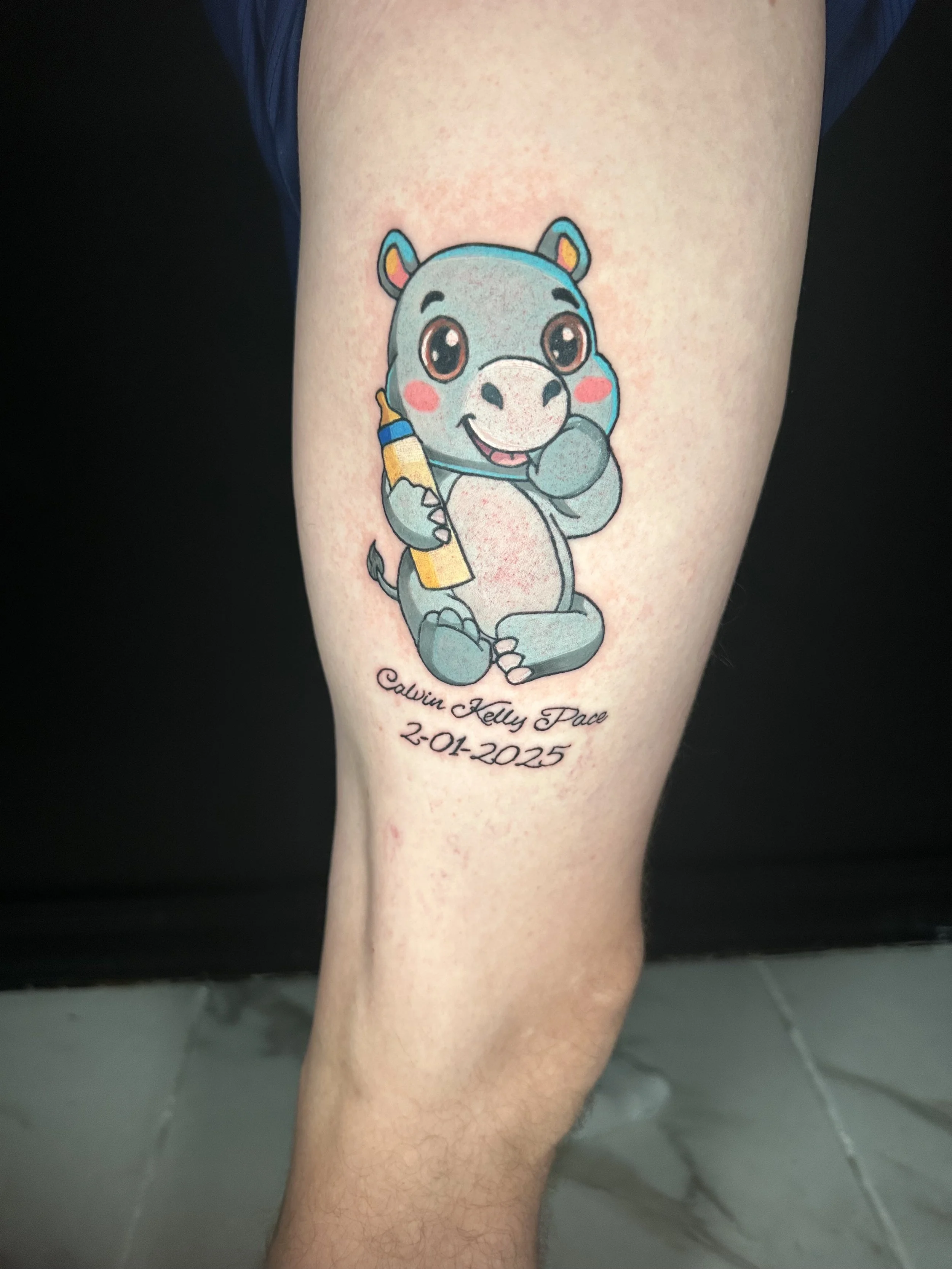 Colorful tattoo of a cartoon bear holding a yellow crayon, with pink cheeks, large expressive eyes, and a playful smile. There is black cursive script with a name and date below the bear.