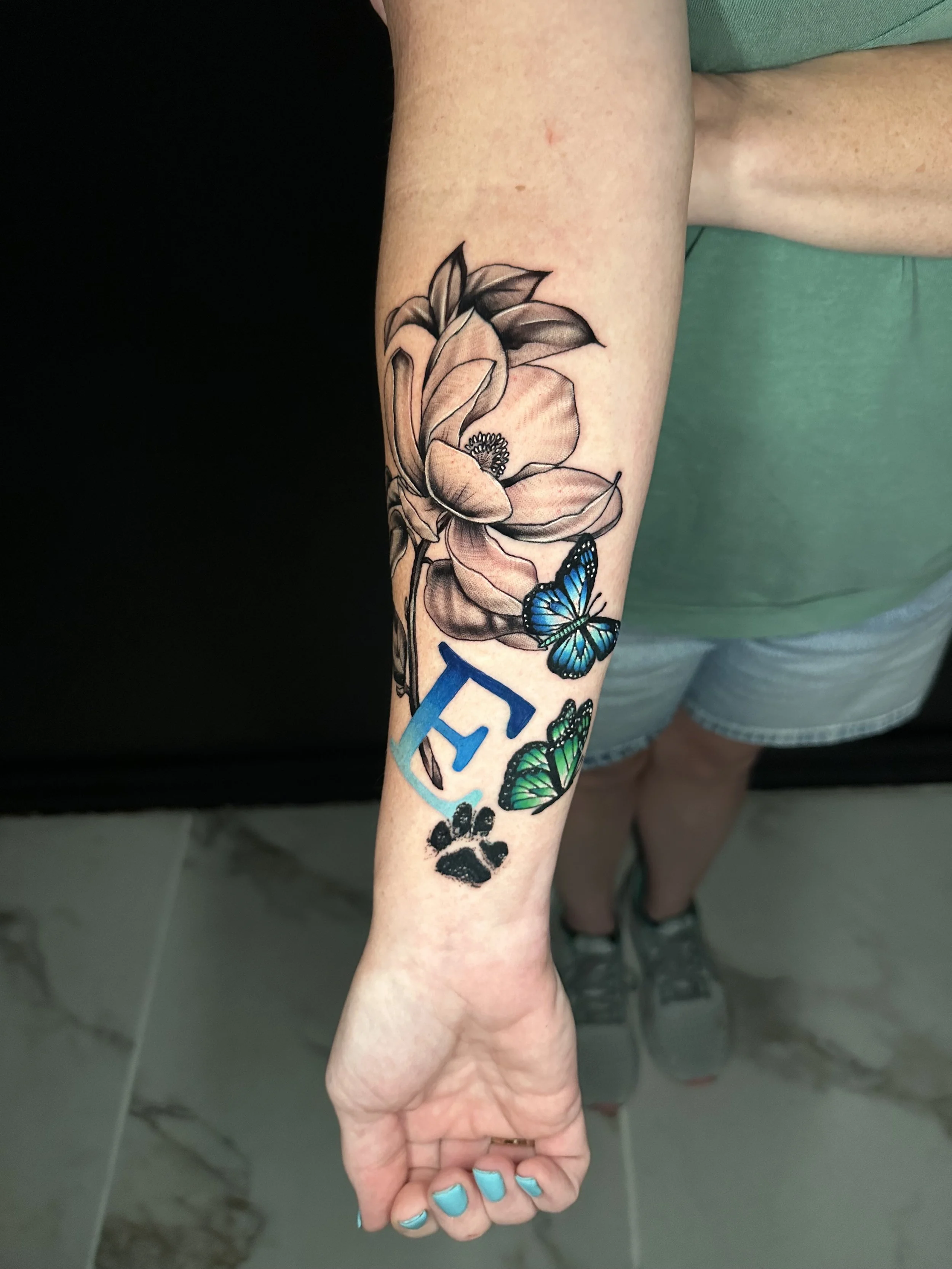 Tattoo on inner forearm featuring a large flower with two butterflies and the word 'PEACE' with a paw print below.